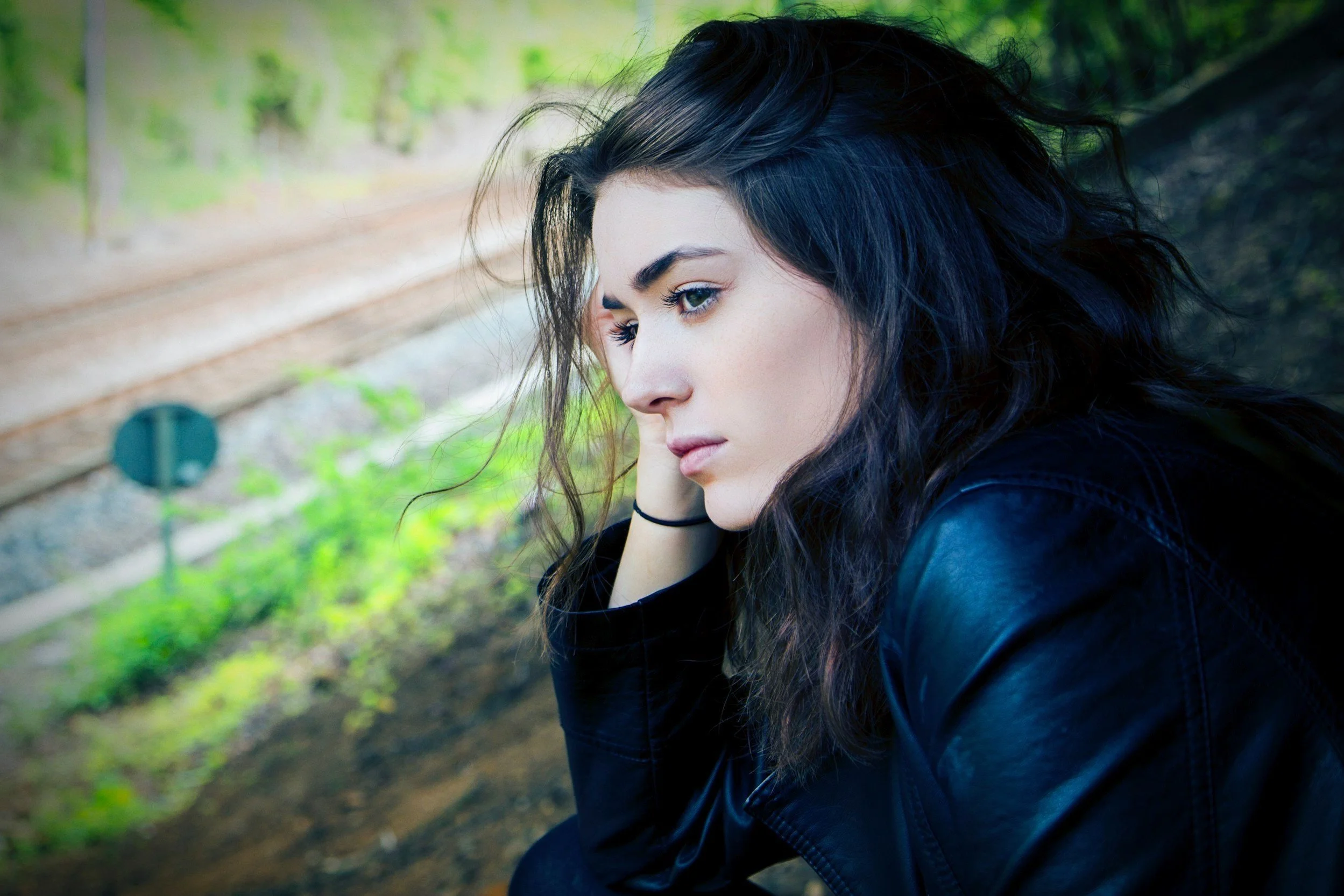 Woman sitting thoughtfully beside train tracks, reflecting on the uncertainty of her fertility journey.