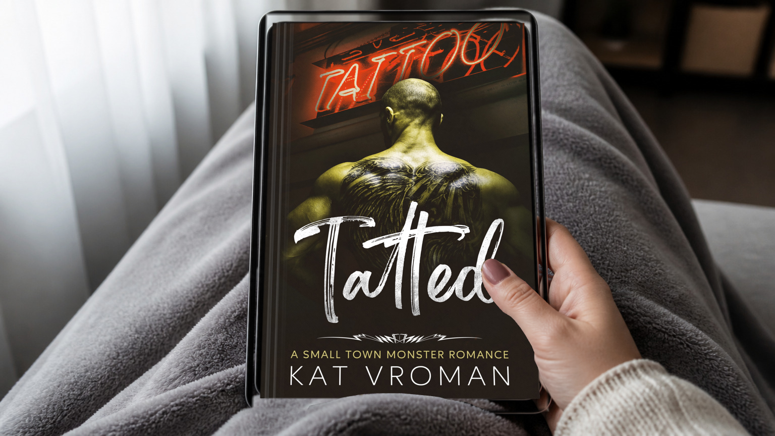 Tatted bys Kat Vroman on tablet held by woman's hand with blanketed lap