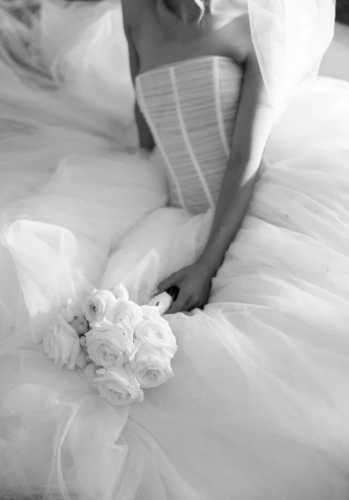 A woman in a wedding dress holding a bouquet of white roses on a bed.