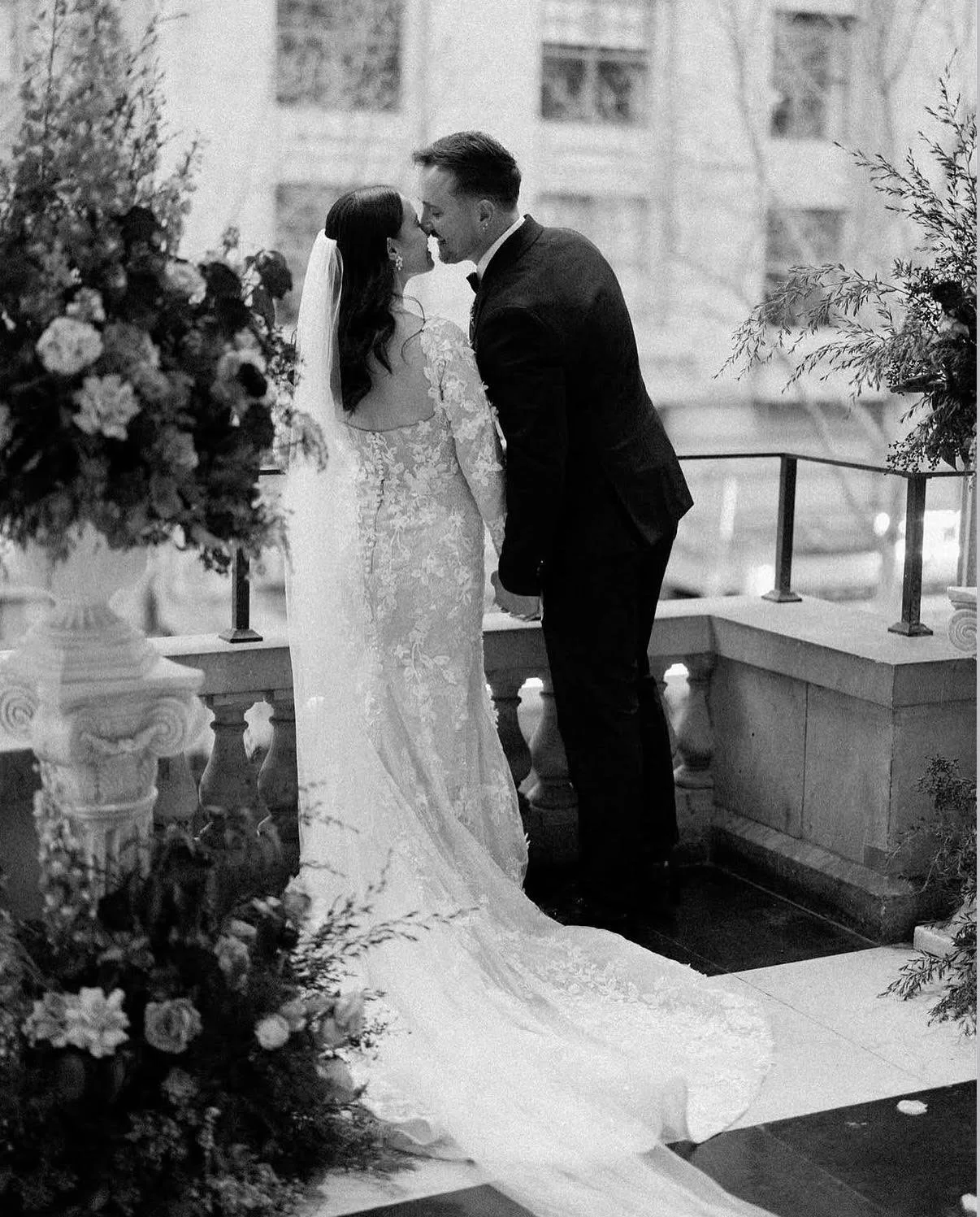 A bride and groom are facing each other, about to kiss during their wedding ceremony, with floral arrangements on either side.