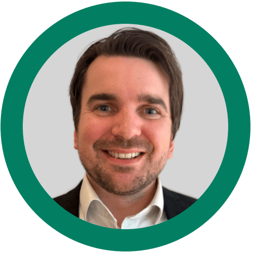 Porträtt av en ung man med mörkt hår och skägg, iklädd en rutiga skjorta och mörk tröja, mot en ljusbakgrund.