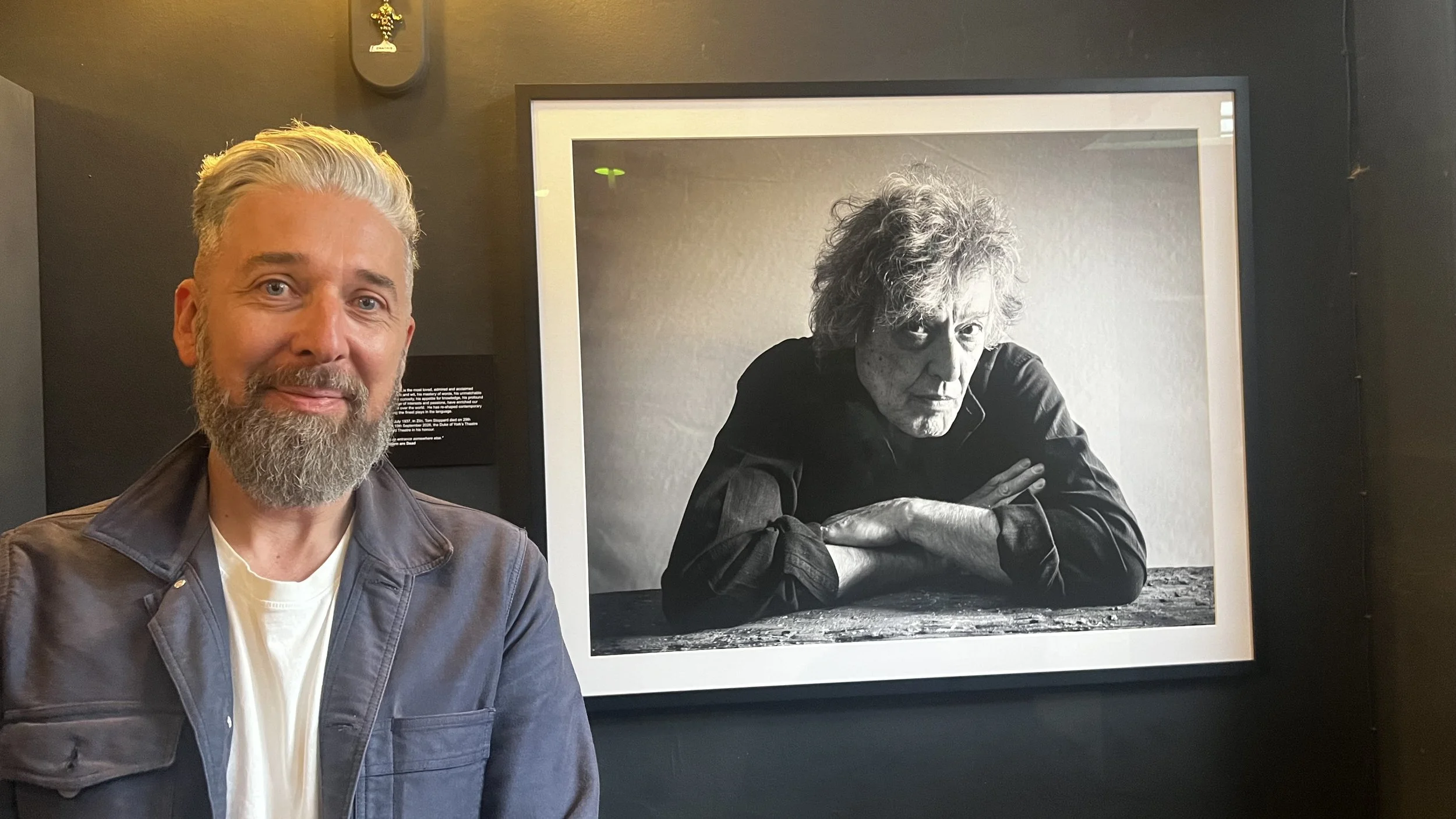 Man standing next to a black and white portrait photograph of another man with his arms folded.