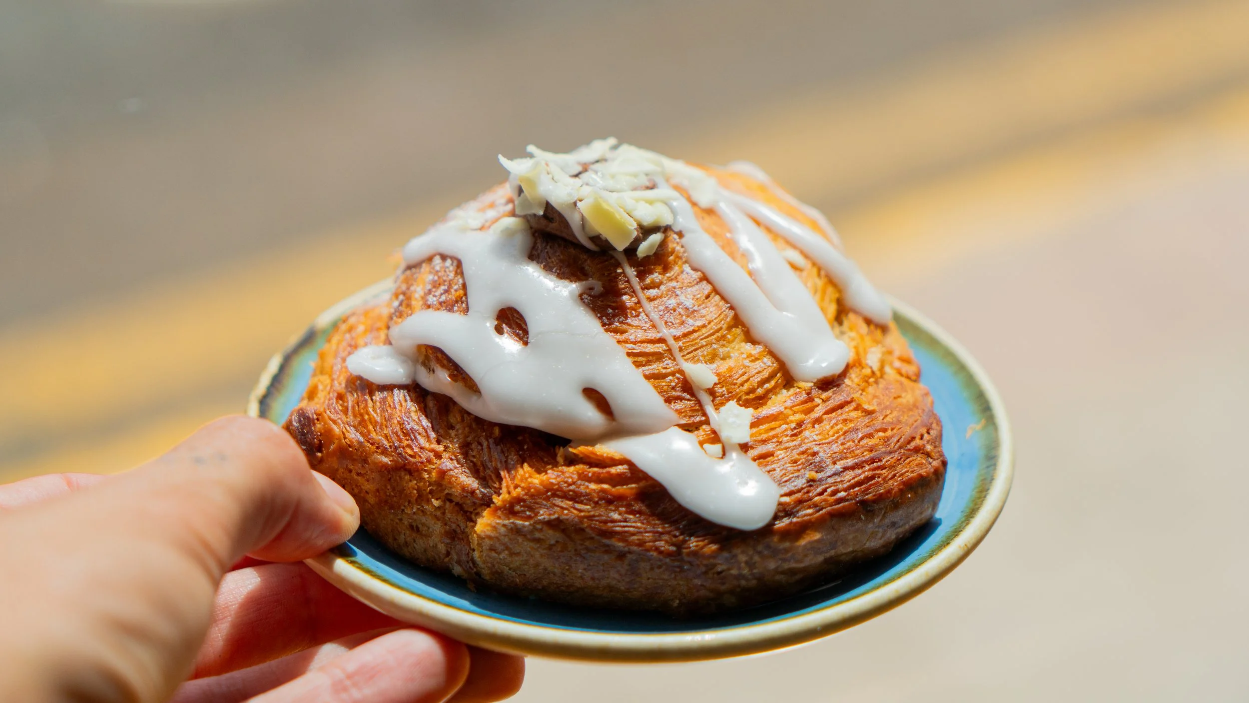Una mano sostiene un plato con un rollo de canela cubierto con glaseado y decorado con trozos de nueces.