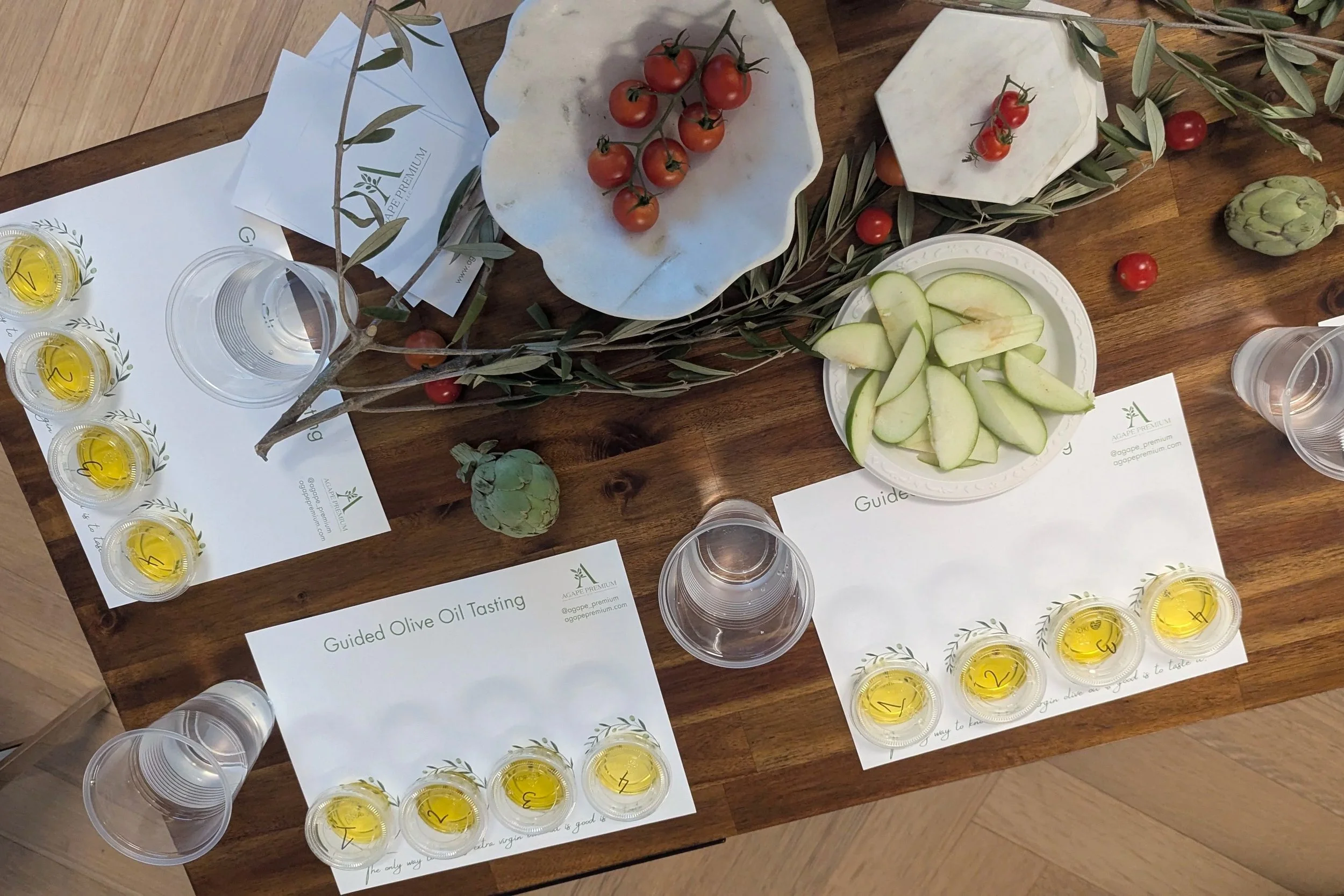 a guided olive oil tasting with olive oil tasting mats on a wooden table with olive branches and green apples and tomato plans and artichokes