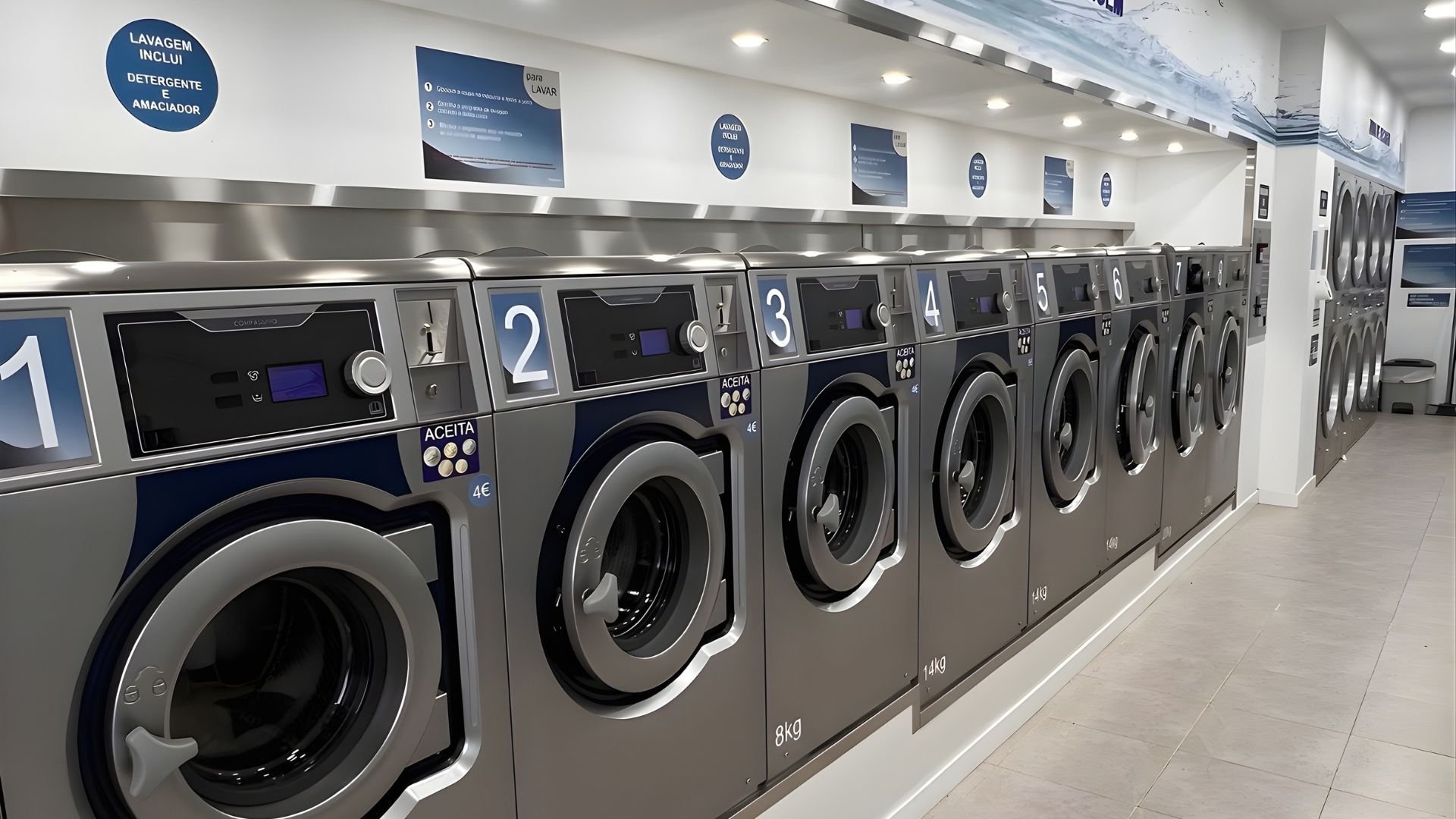 Interior de uma lavandaria self-service moderna, com várias máquinas de lavar e secar alinhadas, identificadas por números, num espaço amplo, limpo e bem iluminado.