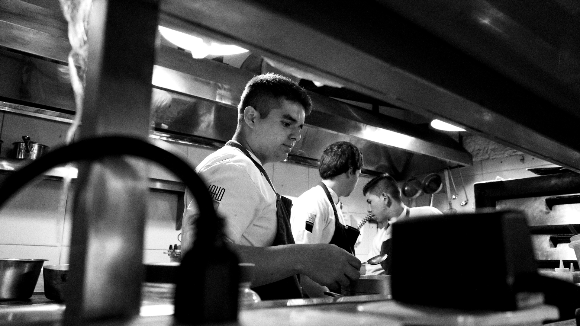 Três profissionais a trabalhar numa cozinha de restaurante, numa fotografia a preto e branco.