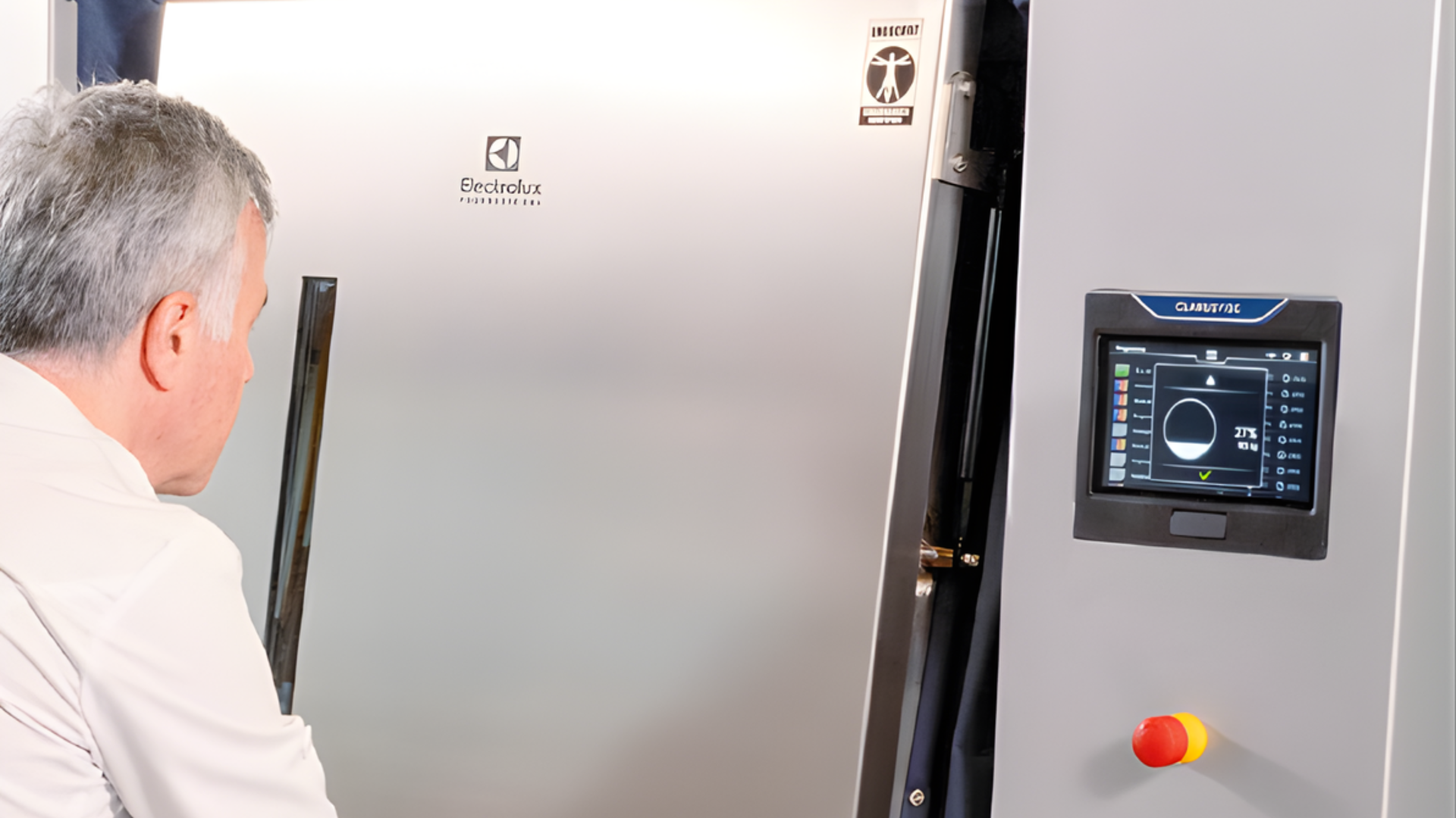 Técnico em bata observa um equipamento de lavandaria profissional Electrolux Professional, com painel de controlo digital (touchscreen) visível na lateral da máquina.