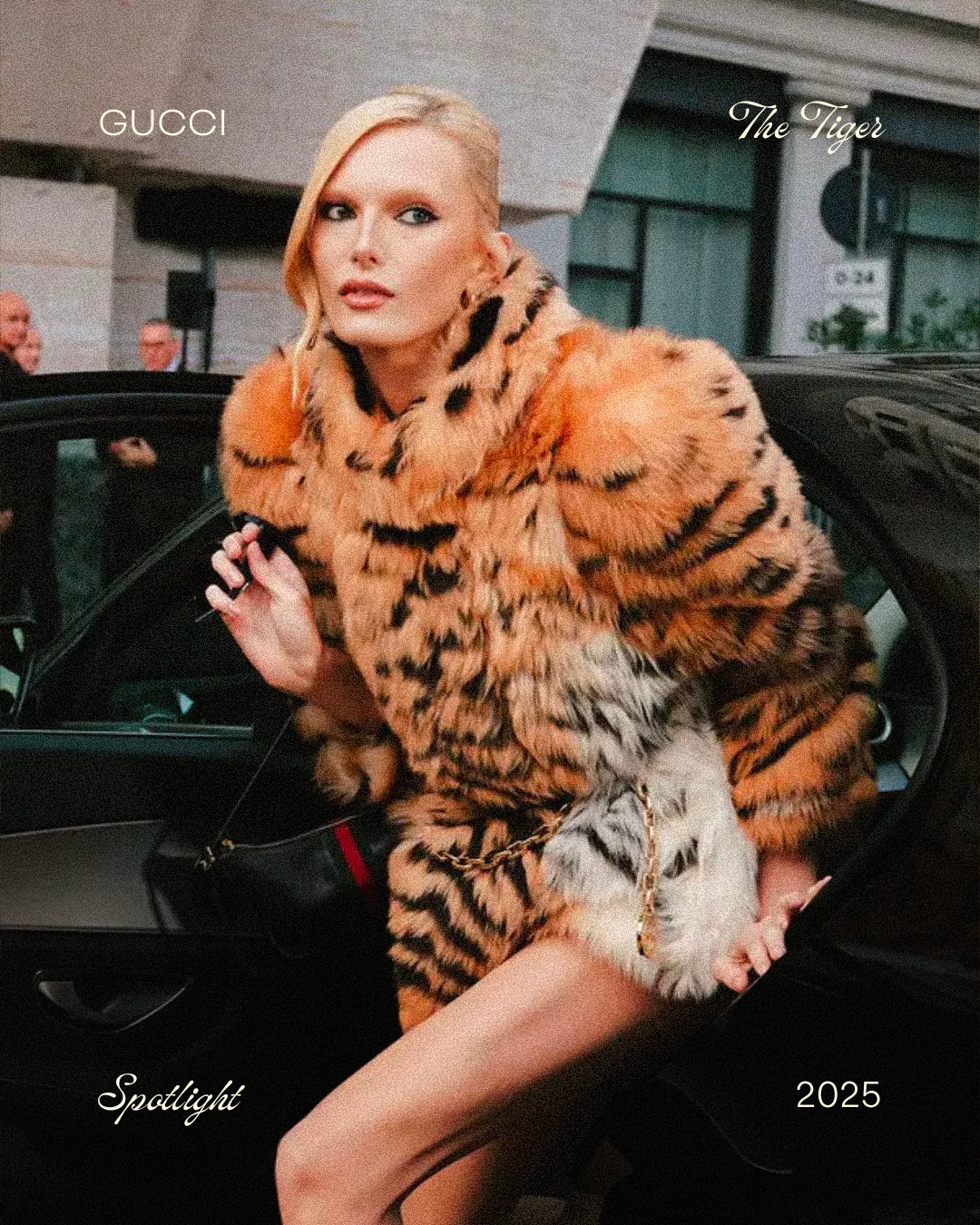A woman with blonde hair in a slicked-back style, wearing a tiger print fur coat, sitting in a black car. The background features a building and a few people. Text on the image includes 'GUCCI,' 'The Tiger,' 'Spotlight,' and '2025.'