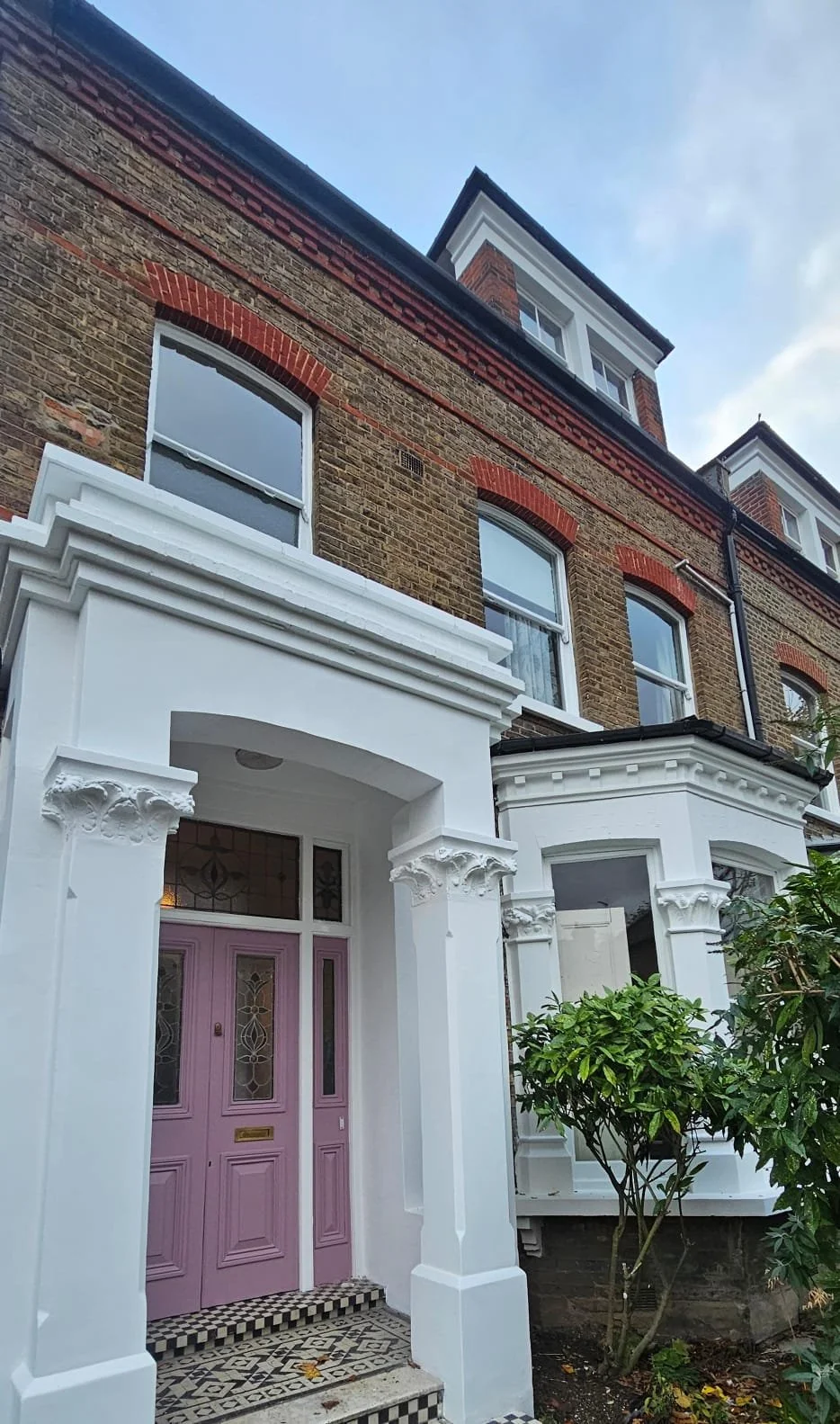 Outdoor patio with glass table, wicker chairs, brown wooden fence, and green plants.