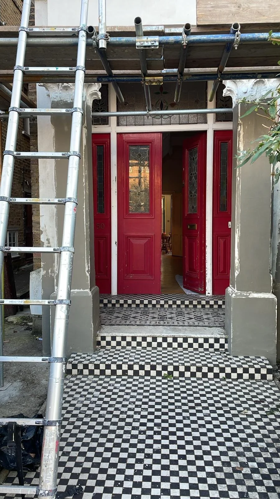 Backyard patio with garden bed, small table, chairs, hot tub, gravel pathway, and string lights overhead, with trees and neighboring houses in the background.