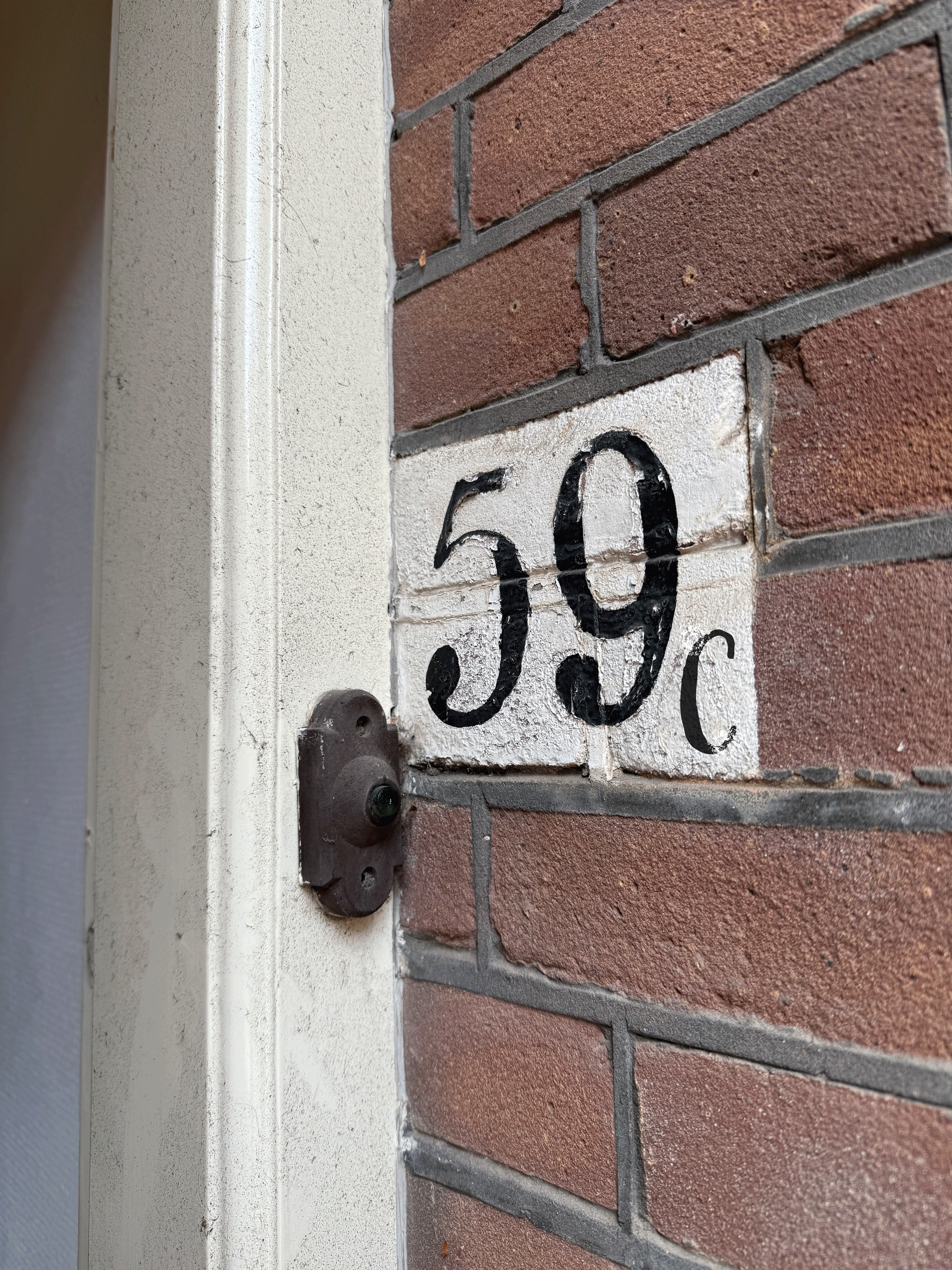 House number plaque displaying '50' painted in black on a white background attached to a brick wall.