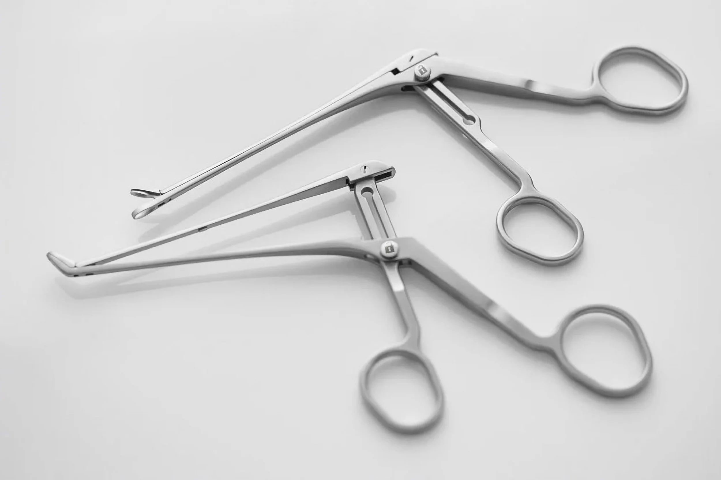 A close-up photograph of two surgical instruments placed on a clean surface. The stainless steel finish, angled tips, and precise hinge mechanisms highlight their functionality and the high standards of medical-grade design.