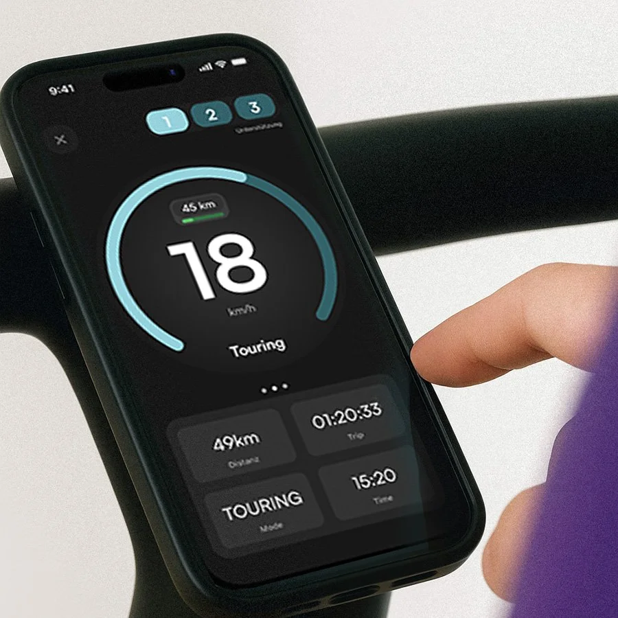 A person using a smartphone to monitor e-bike ride stats, showing 18 km/h speed, 49 km distance, 1 hour 20 minutes trip, and 15 minutes 20 seconds time, on a cycling display.