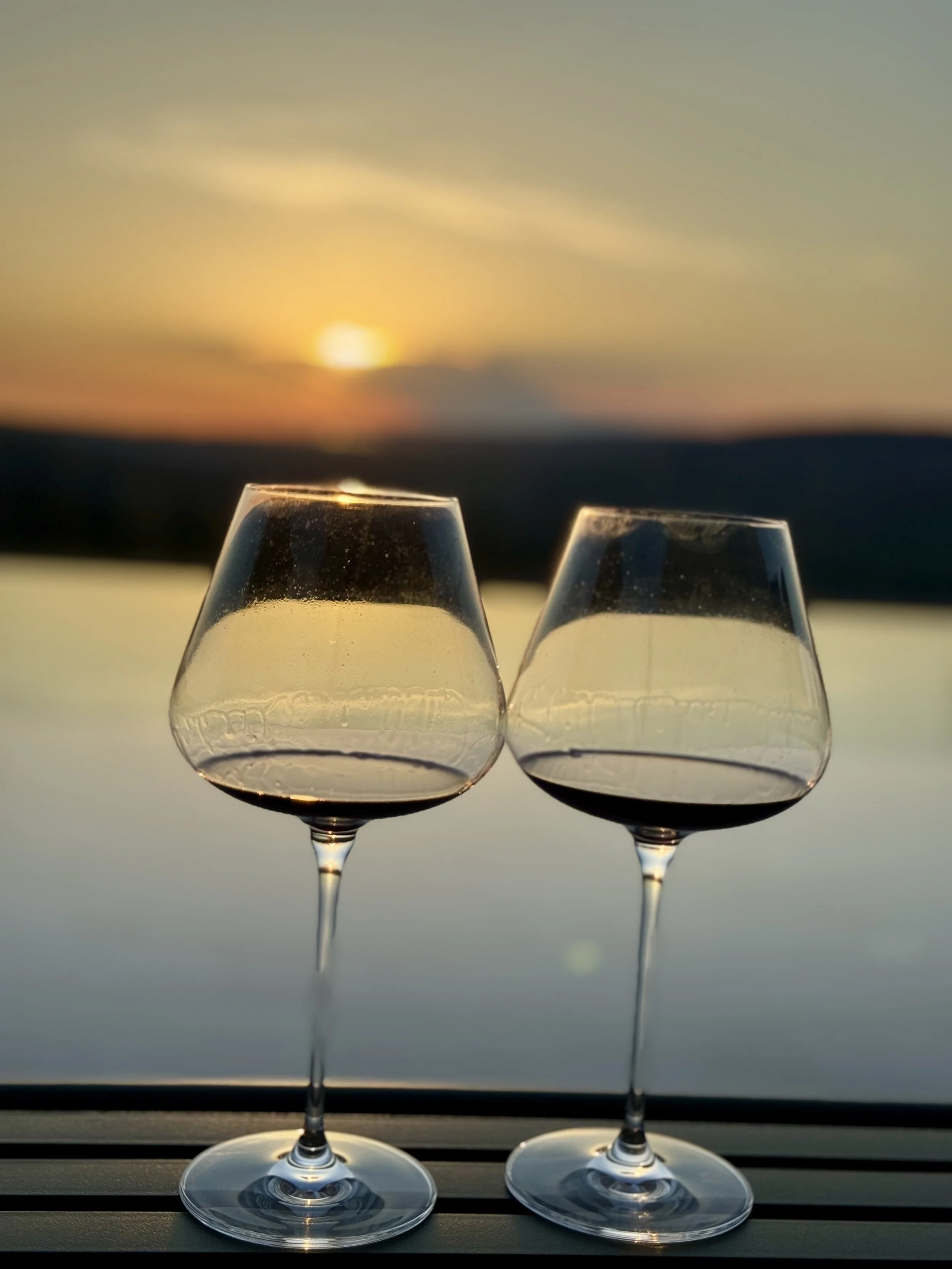 Two glasses of red wine clinking softly against a golden Istrian sunset backdrop