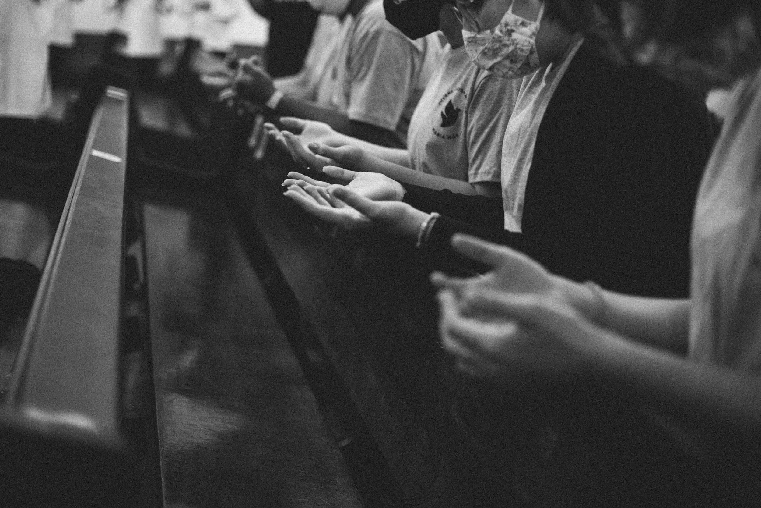 People sitting in a row, hands outstretched in prayer.