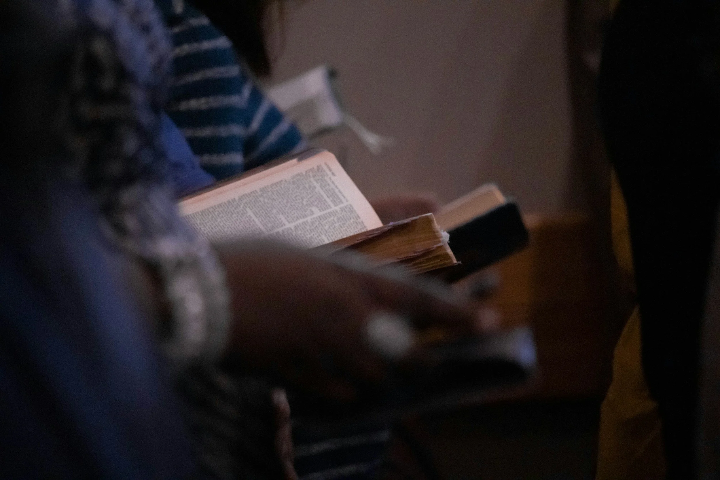 Close-up of a person reading a Bible, in a dimly lit setting.