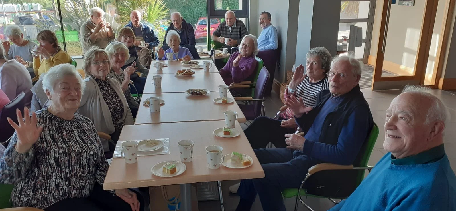 Group of elderly people enjoying a meal and coffee together in the church welcome area, a well-lit room with large windows.