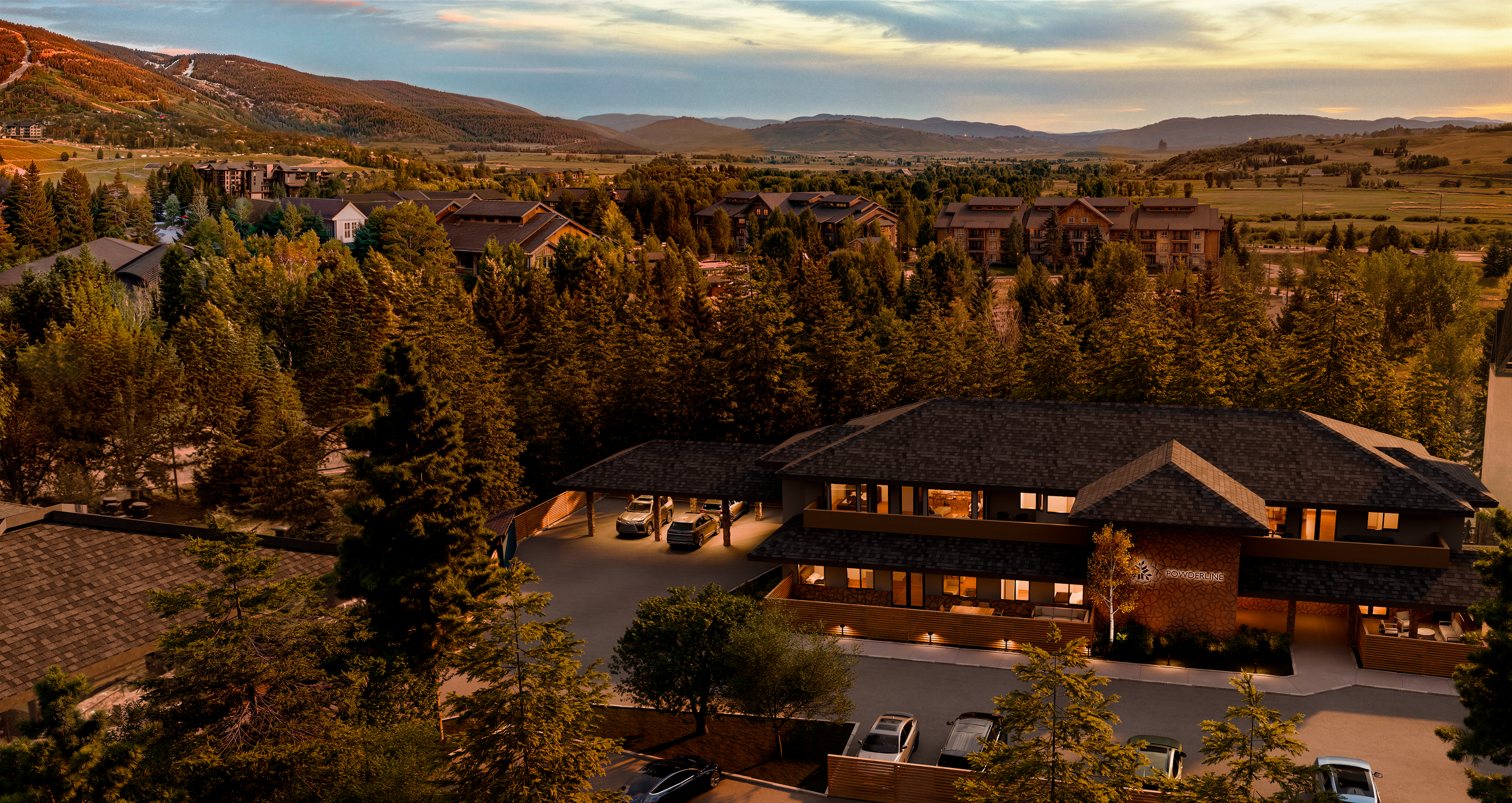 A scenic view of a mountain resort town during sunset, with a mix of residential buildings, a modern lodge in the foreground, and distant mountains and forests in the background.