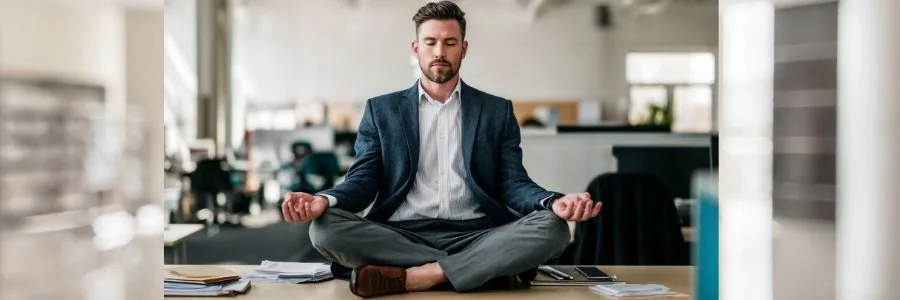 Man meditating at a desk in a modern office environment, symbolizing the application of mindfulness and inner calm practices in everyday work and modern life.
