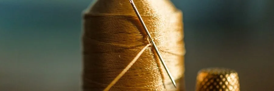 Close-up image of a needle threading golden thread, representing the integration of ancient wisdom and modern science, and how small, intentional practices weave lasting inner calm over time.
