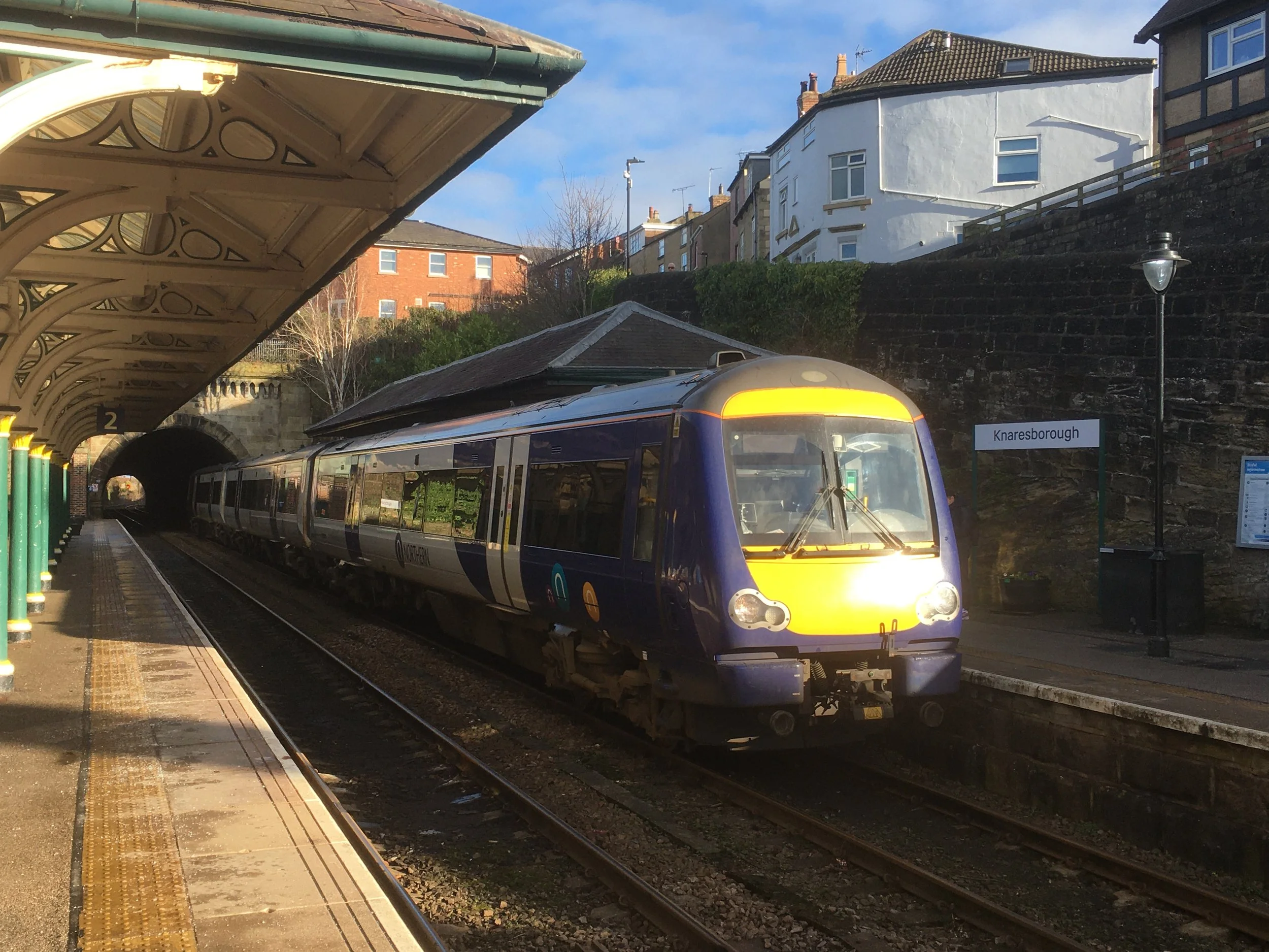 A train at Knaresborough train station on a sunny day with a tunnel in the background.