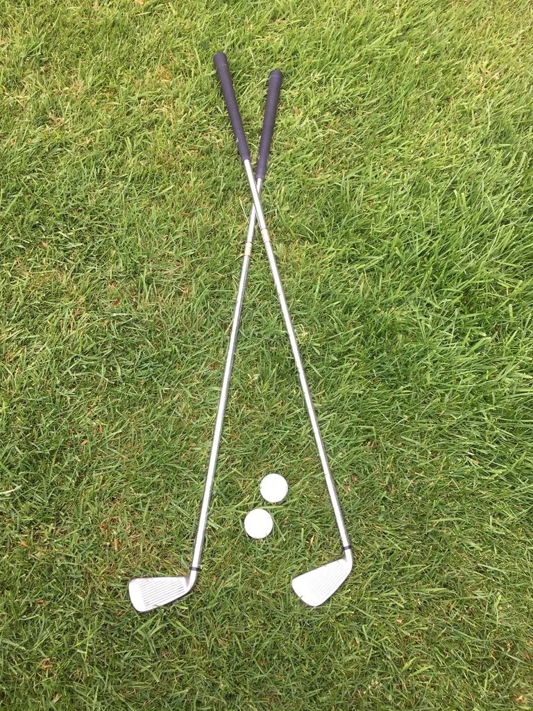 Two golf clubs and two golf balls on a grassy field.