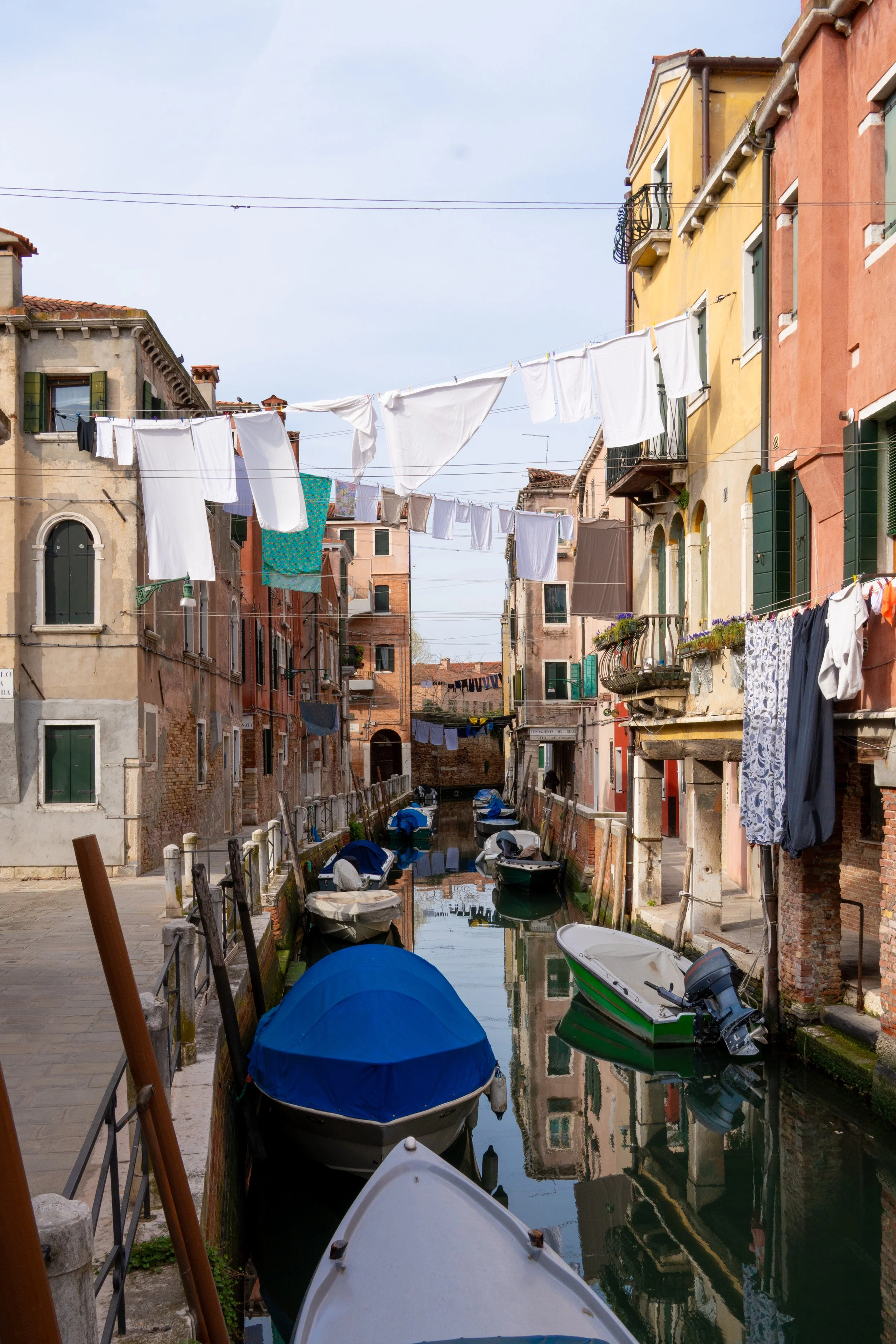 Colorful buildings lining a canal with boats, laundry hanging on lines overhead in Venice, Italy.