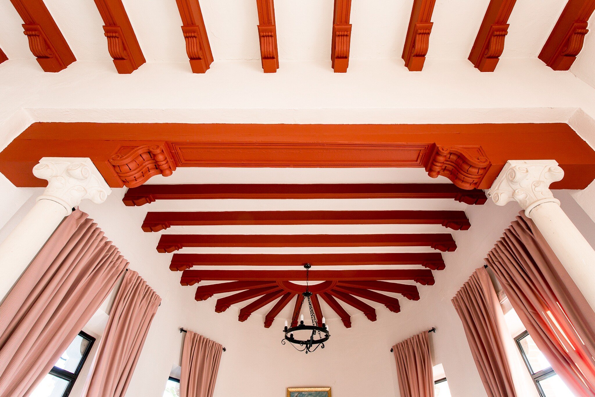Detail of ceiling with red wooden beams and large windows.