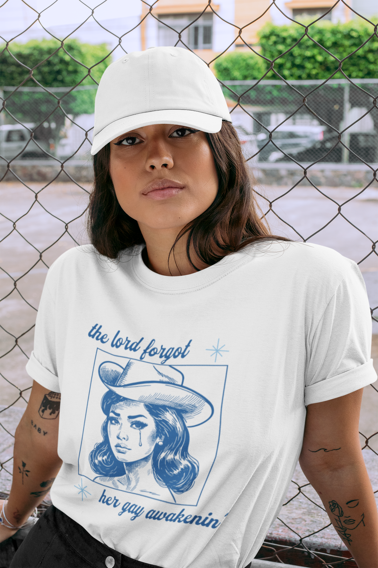 t-shirt-mockup-featuring-a-woman-wearing-a-dad-hat-by-a-chain-link-fence-28600.png