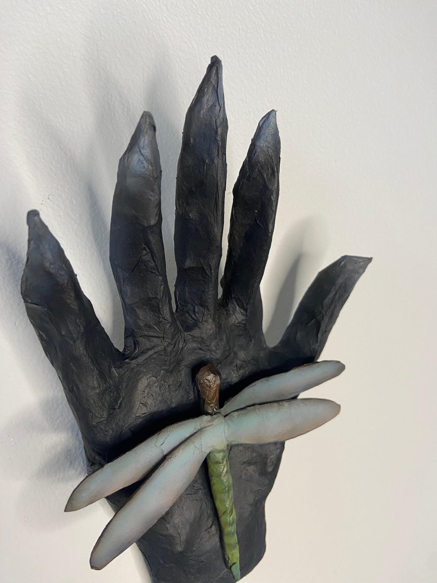 Transformation sculpture depicting a hand and dragonfly, crafted from repurposed materials