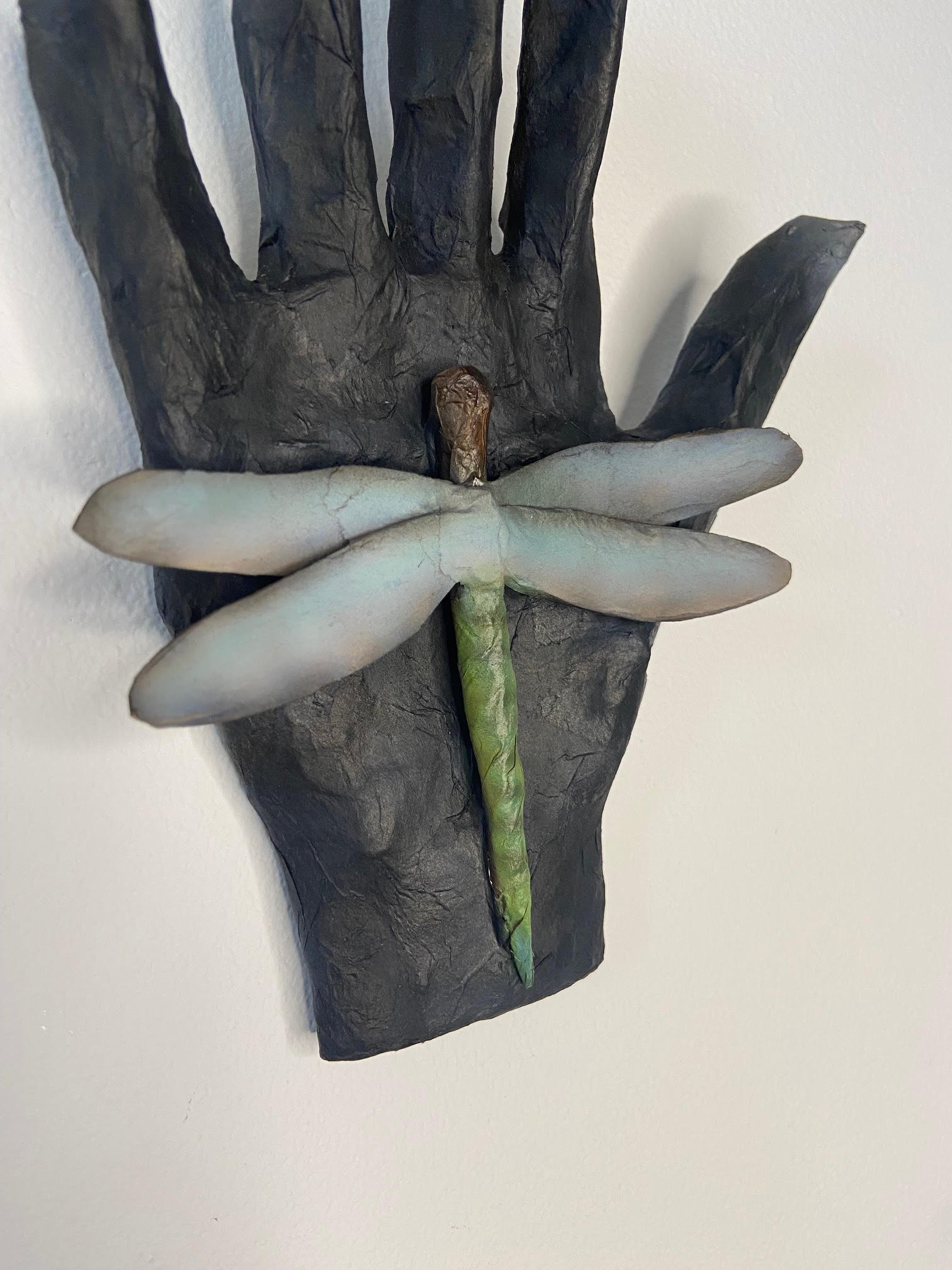 Transformation sculpture depicting a hand and dragonfly, crafted from repurposed materials