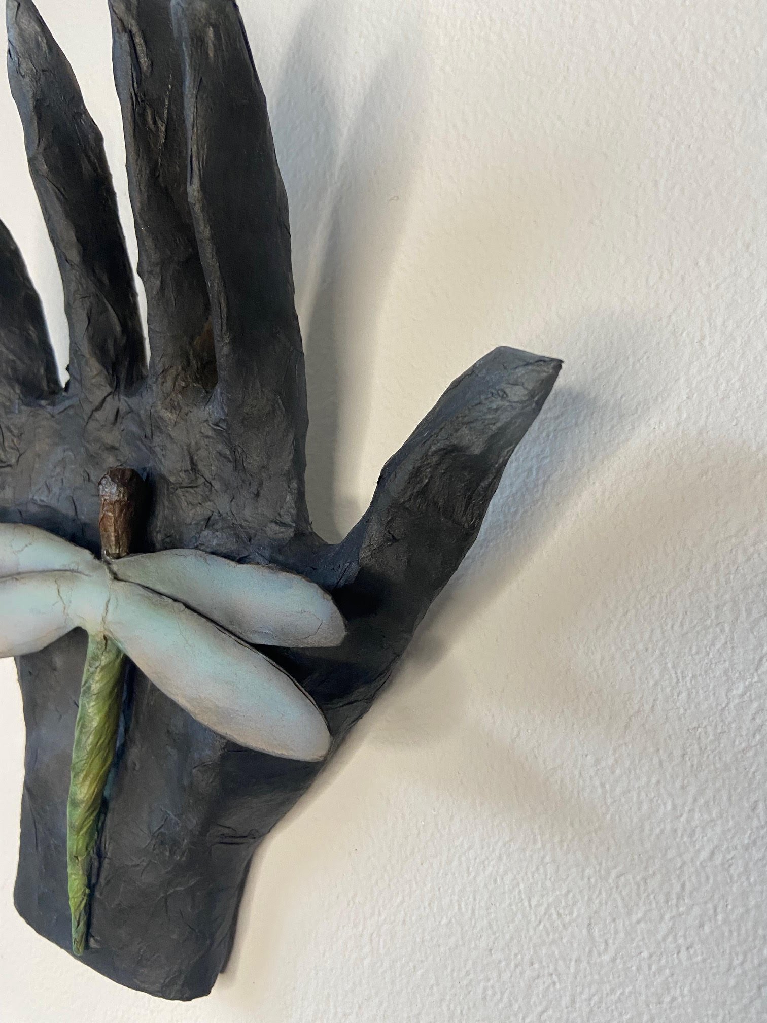Transformation sculpture depicting a hand and dragonfly, crafted from discarded paper materials