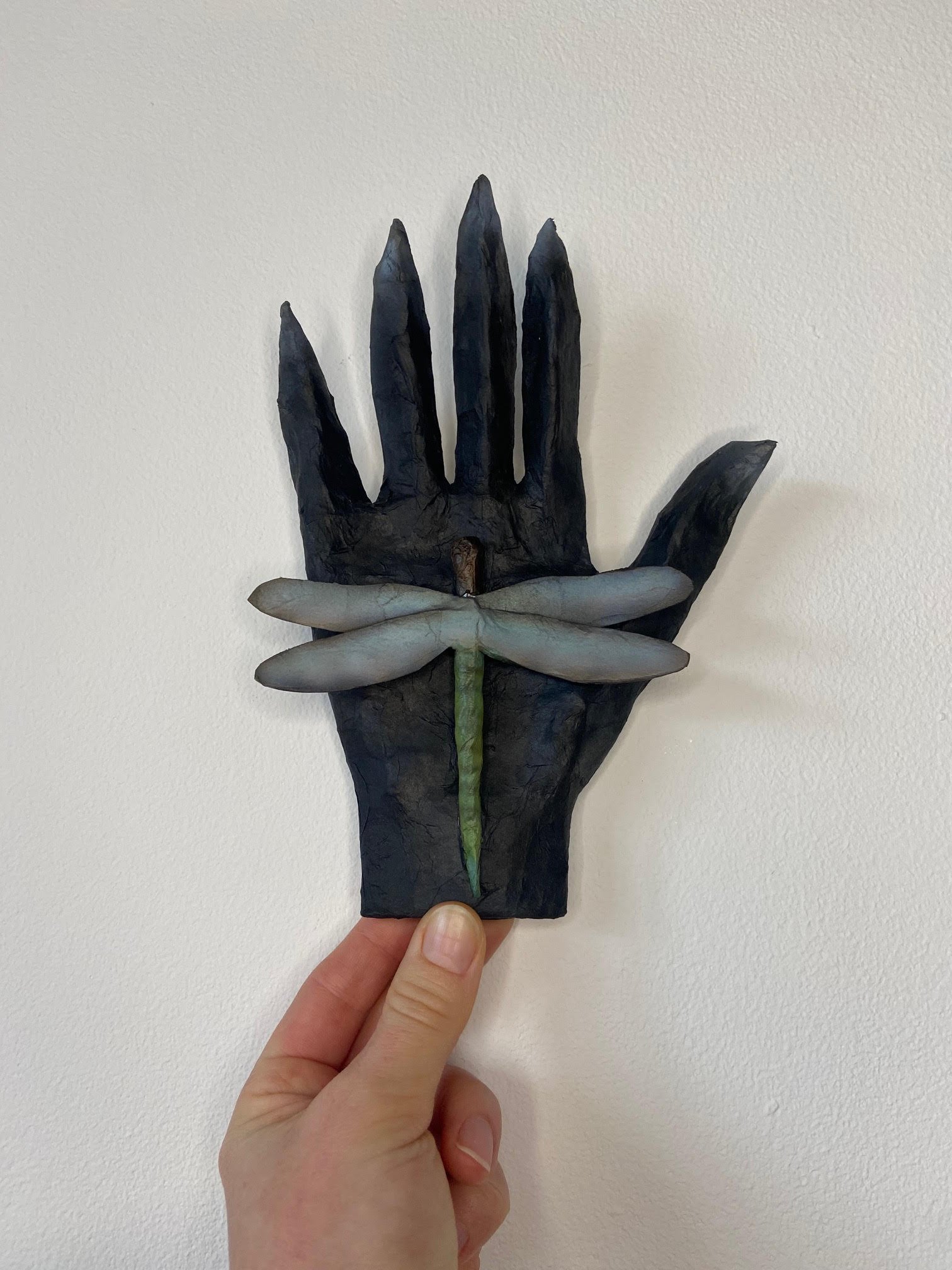 Transformation eco-conscious sculpture depicting a hand and dragonfly, crafted from discarded paper materials