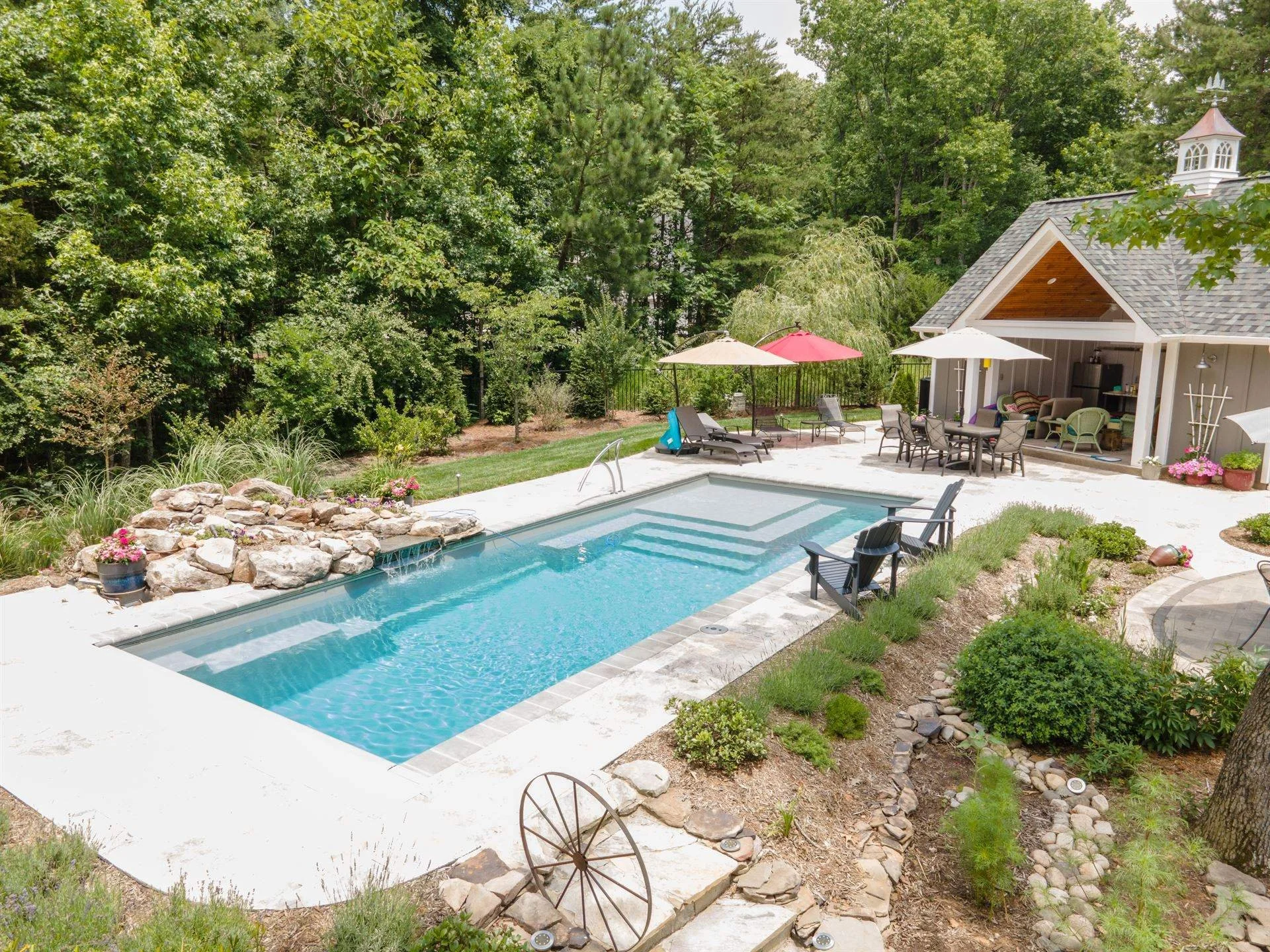 Backyard with a swimming pool in dry ridge, ky, deck chairs, umbrellas, a covered patio with outdoor furniture, and lush trees and plants.