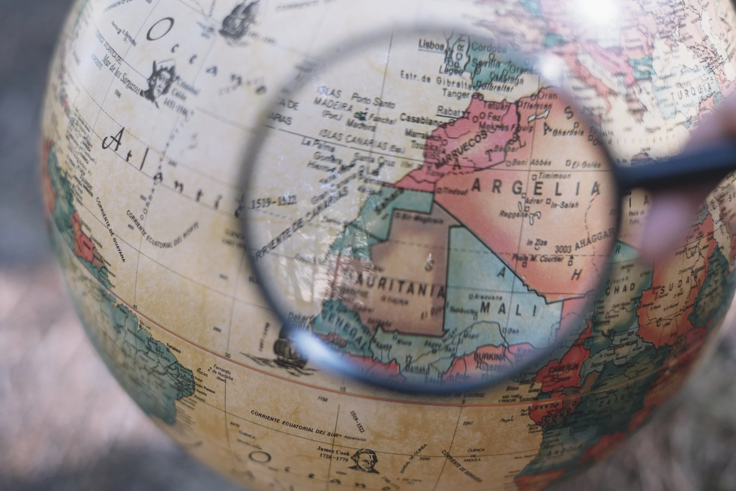 Globe blanc avec loupe sur l’Espagne et la côte ouest africaine, illustrant le chemin de vie 9 : voyage, ouverture, quête d’ailleurs.