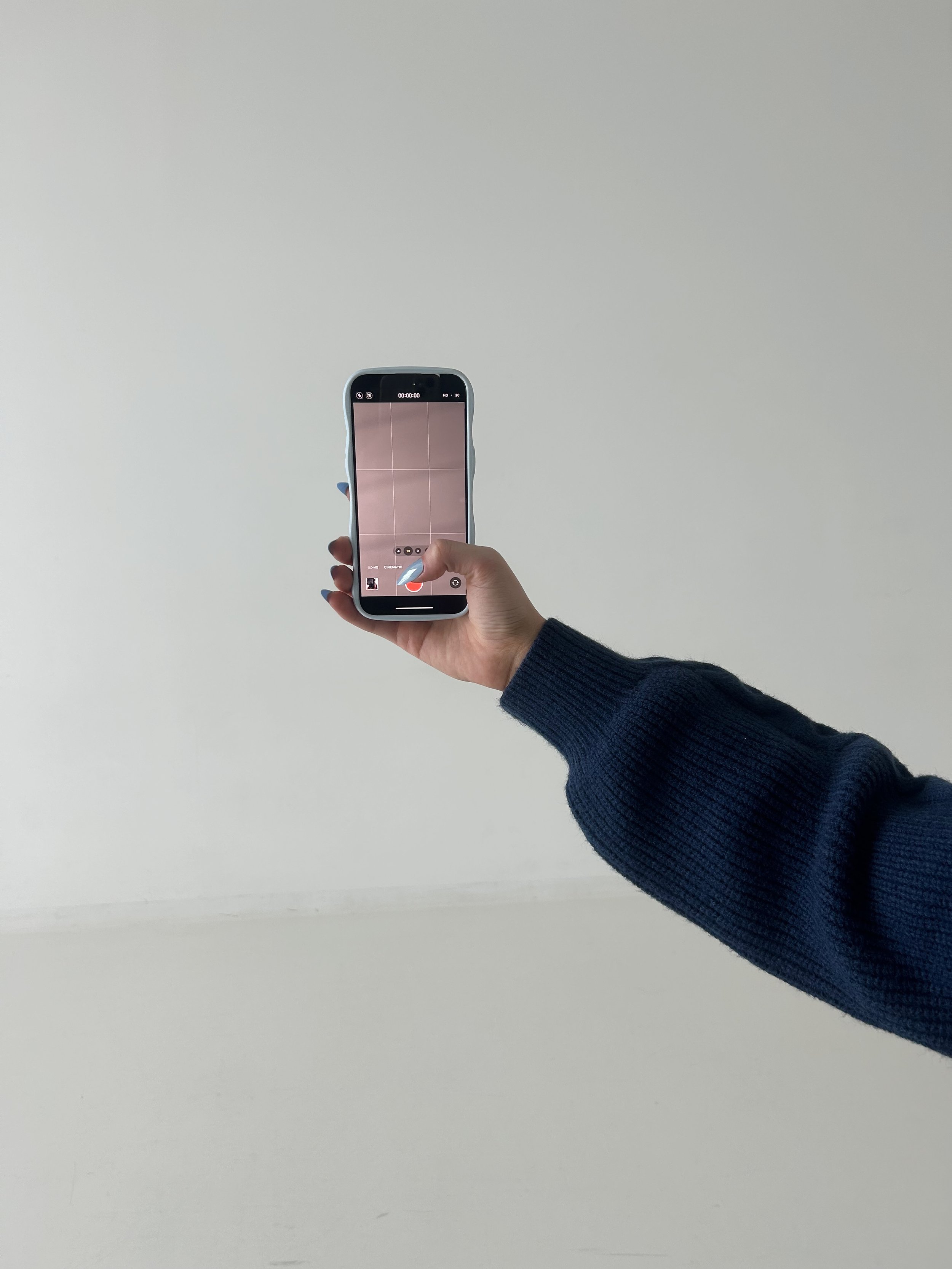 Person holding a smartphone, taking a photo of a plain white wall.