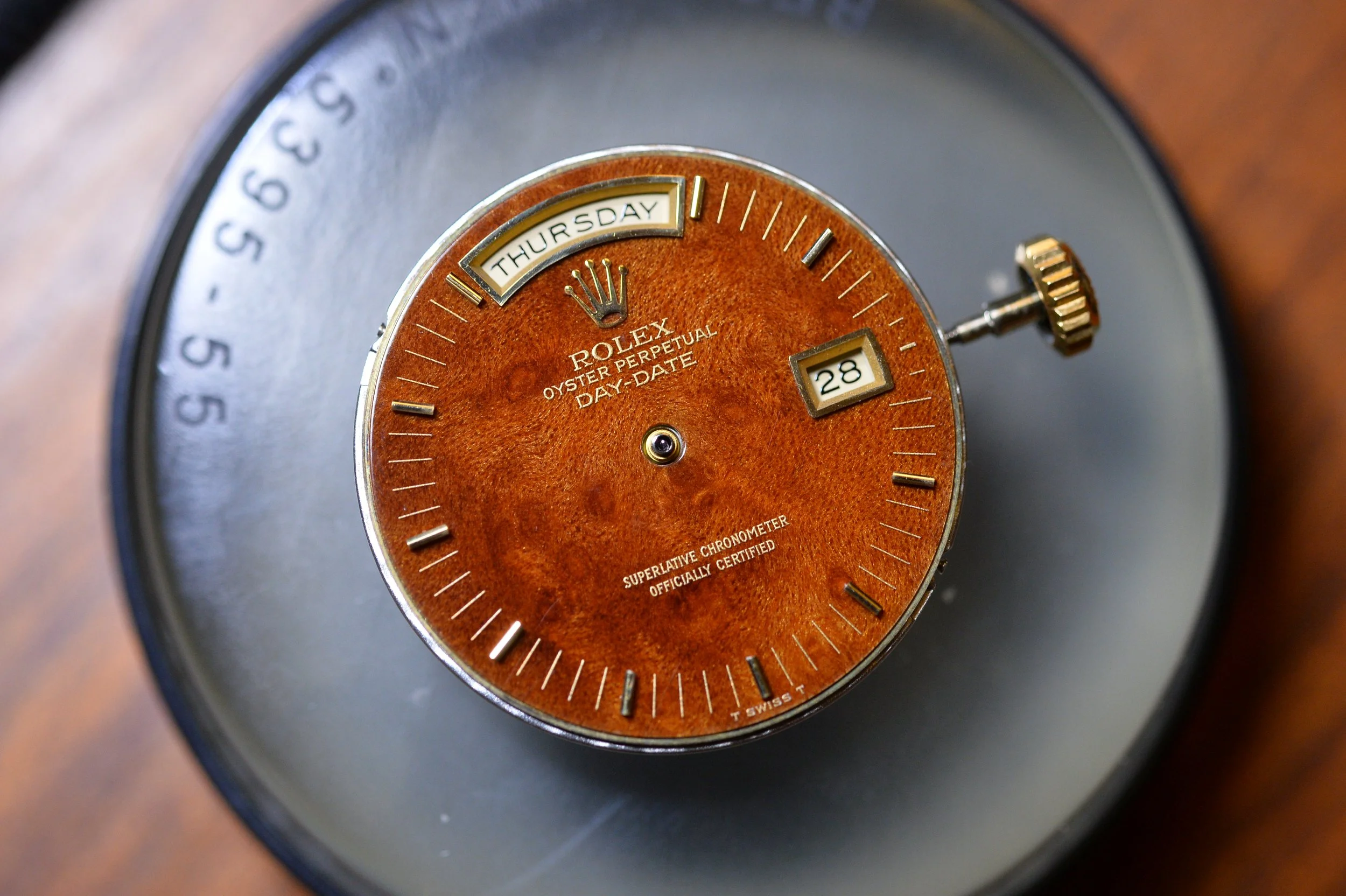 Close-up of a vintage Rolex watch face showing the day as Thursday, the date as 28, with a brown textured background and gold accents.