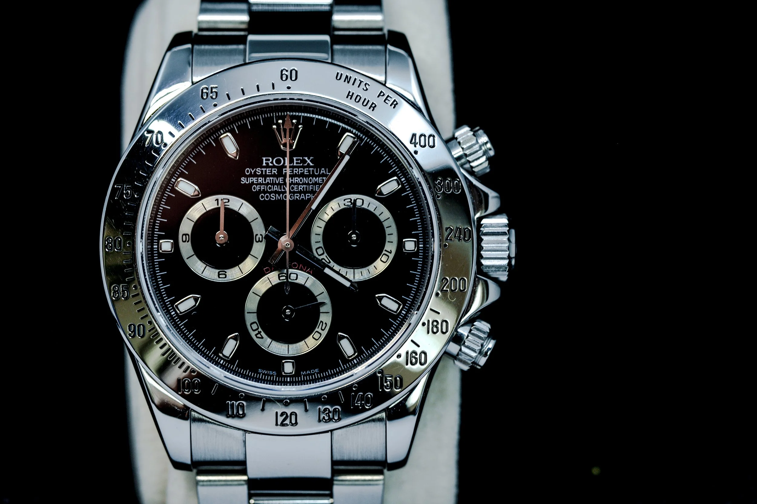 Close-up of a Rolex Cosmograph Daytona wristwatch with a black dial, silver subdials, and a silver tachymeter bezel.
