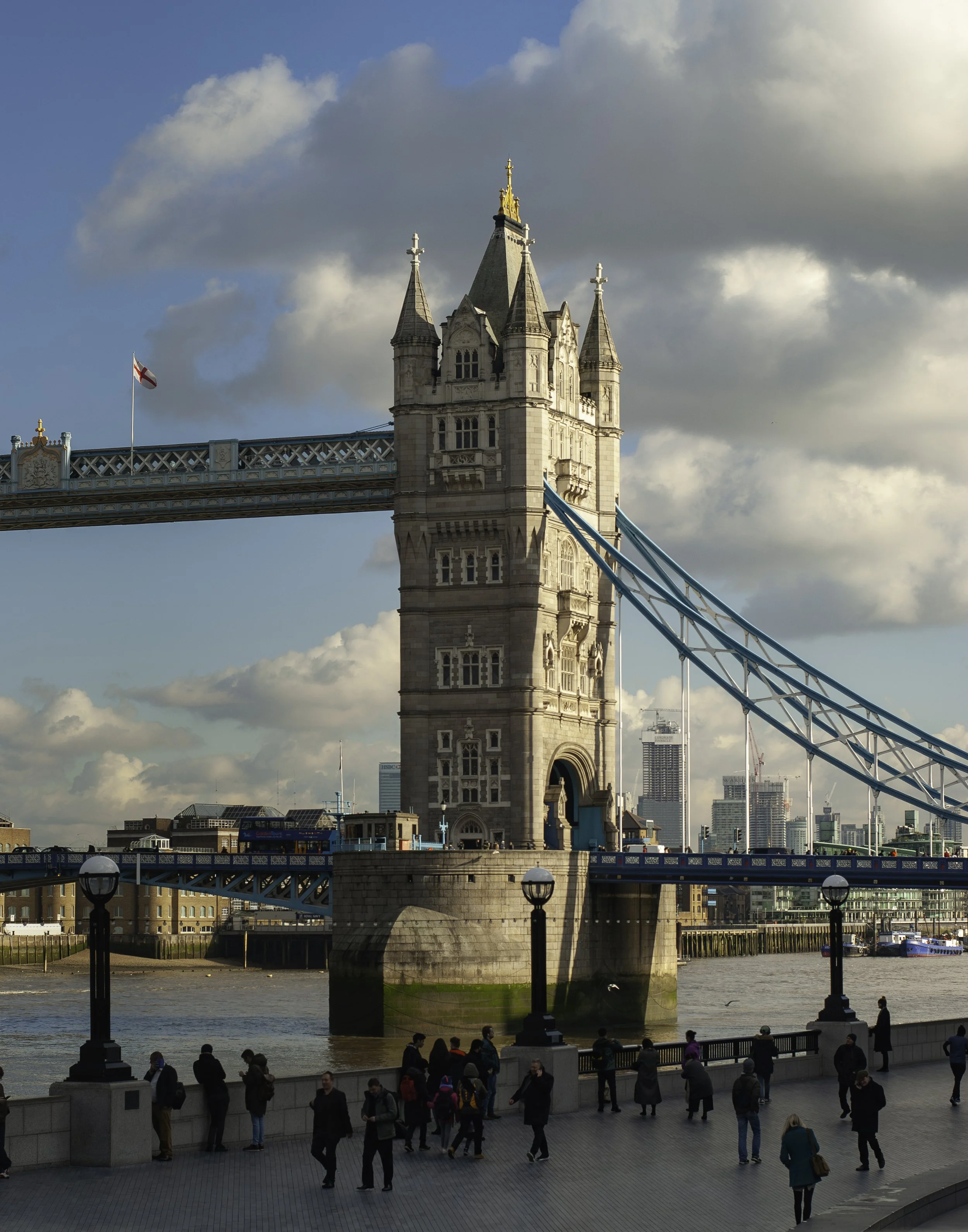 London's Tower Bridge with pedestrians walking along the riverbank.