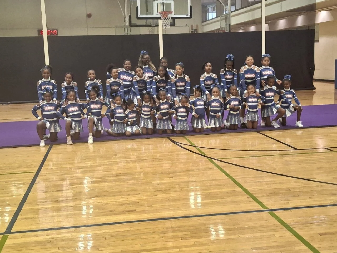 A group of young cheerleaders in blue and silver uniforms posing on a basketball court inside a gymnasium.