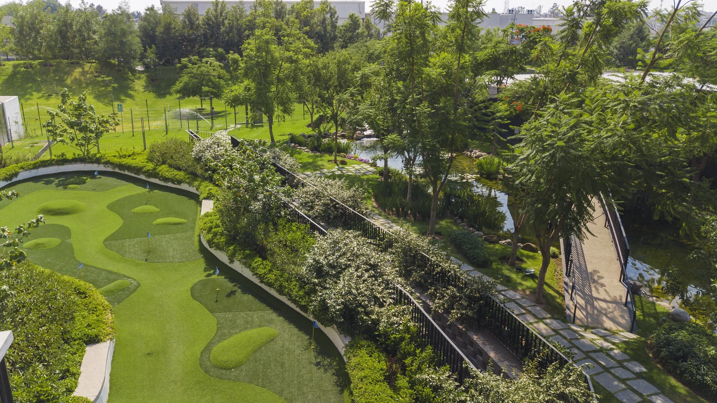 Vista aérea de un parque o jardín con áreas verdes, senderos, árboles y un río o cuerpo de agua pequeño.