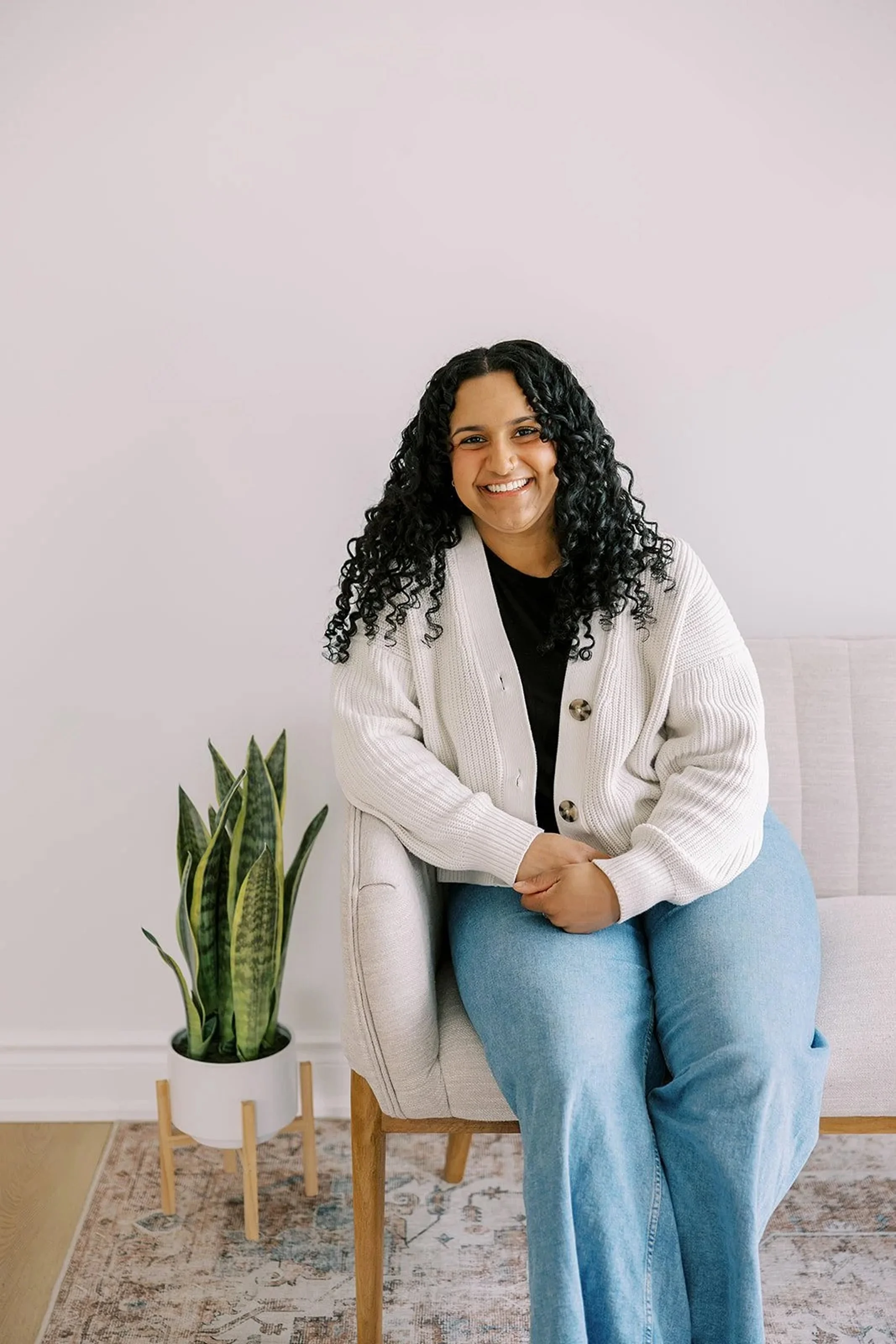 Chriselle Vaz, clinical director, sitting on a sofa in a bright therapy office, smiling. Specialist in couples counseling and relationship therapy