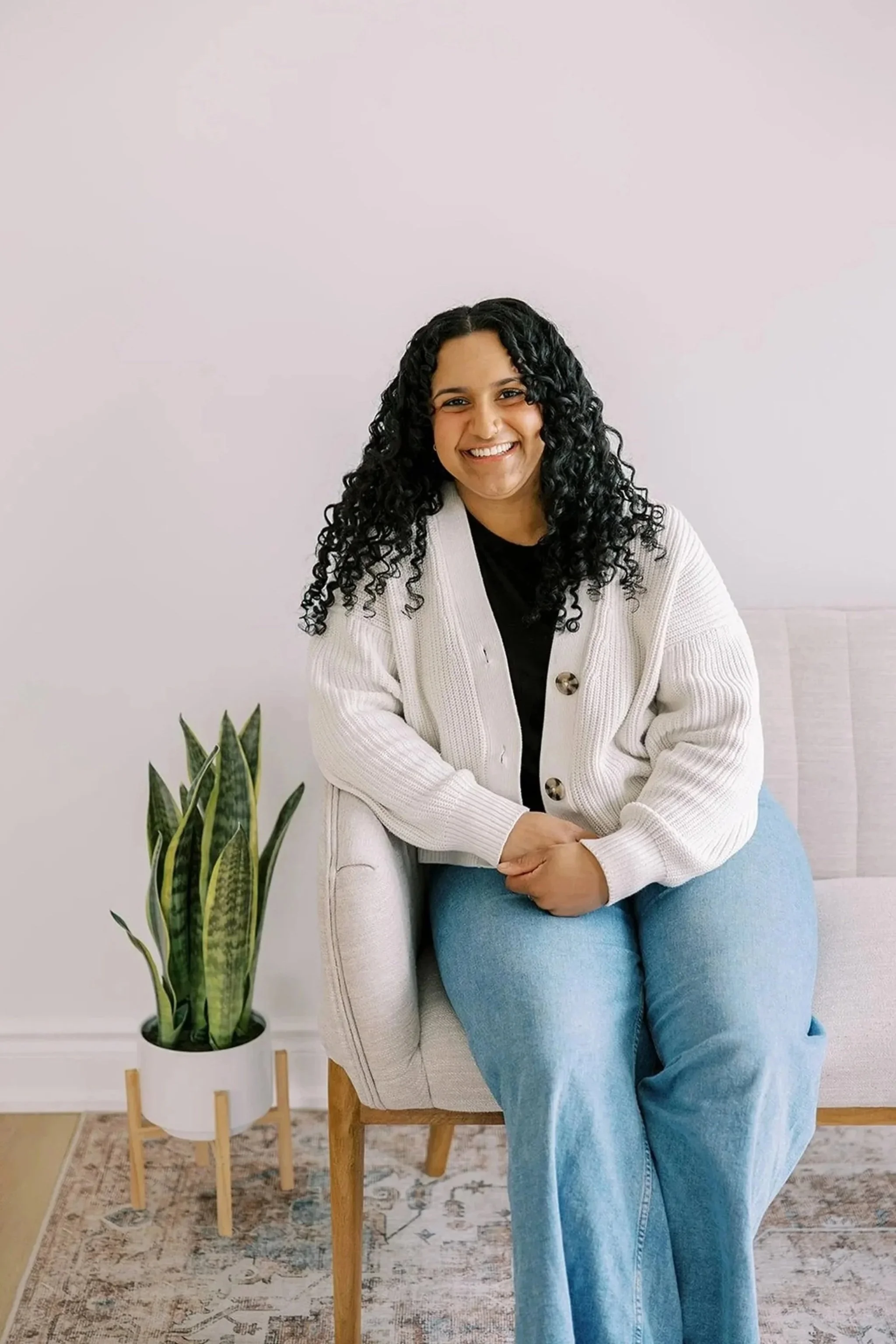 Chriselle Vaz, Clinical Director, sitting on a sofa in a bright therapy office, smiling. Specialist in couples counseling and relationship therapy