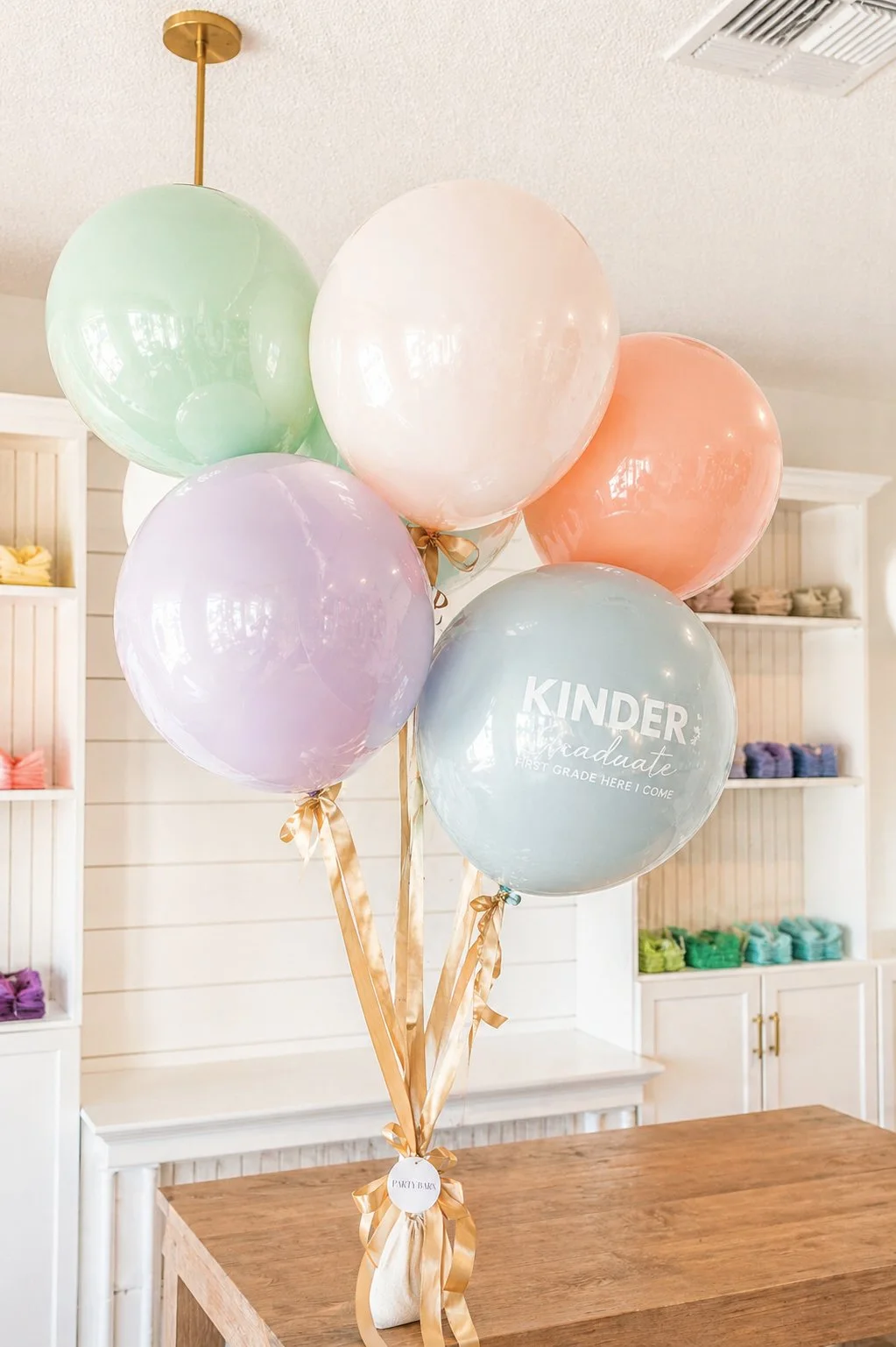 A bouquet of pastel-colored balloons with one balloon displaying the text 'KINDER Graduate First Grade Here I Come' inside a light blue balloon Custom Balloons by Party Barn in Old Town Murrieta