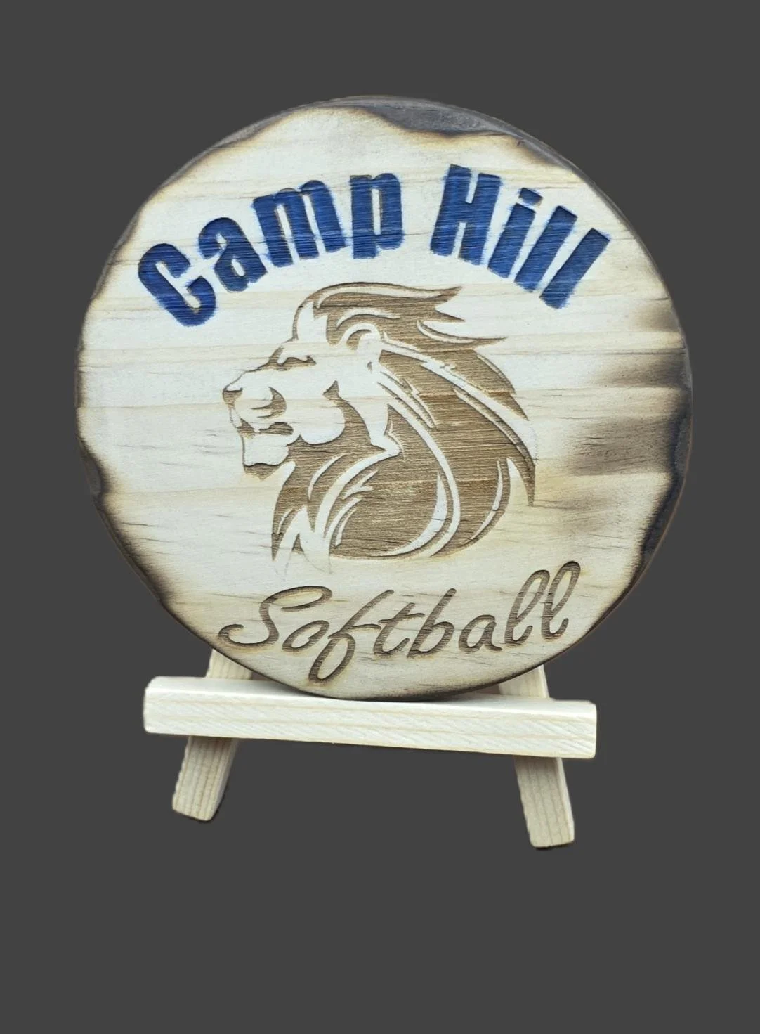 Wooden sign with engraved lion and text "Camp Hill Softball" in blue and brown, displayed on a small easel.