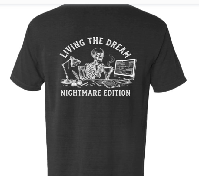 Black T-shirt with a graphic of a skeleton working at a desk, holding a mug. The scene includes a computer, a lamp, and papers. The text reads 'LIVING THE DREAM' above and 'NIGHTMARE EDITION' below.