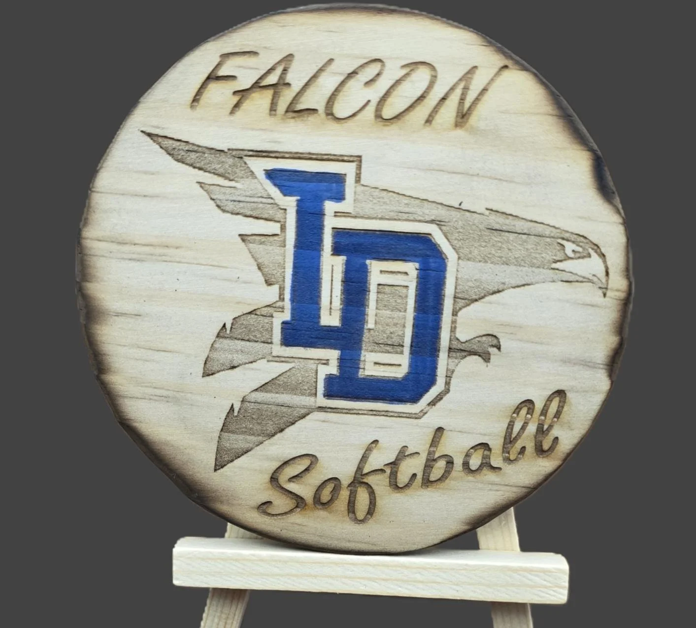 Wooden plaque with logo of a falcon and the text 'Falcon Softball' in blue and brown, mounted on a small wooden stand.