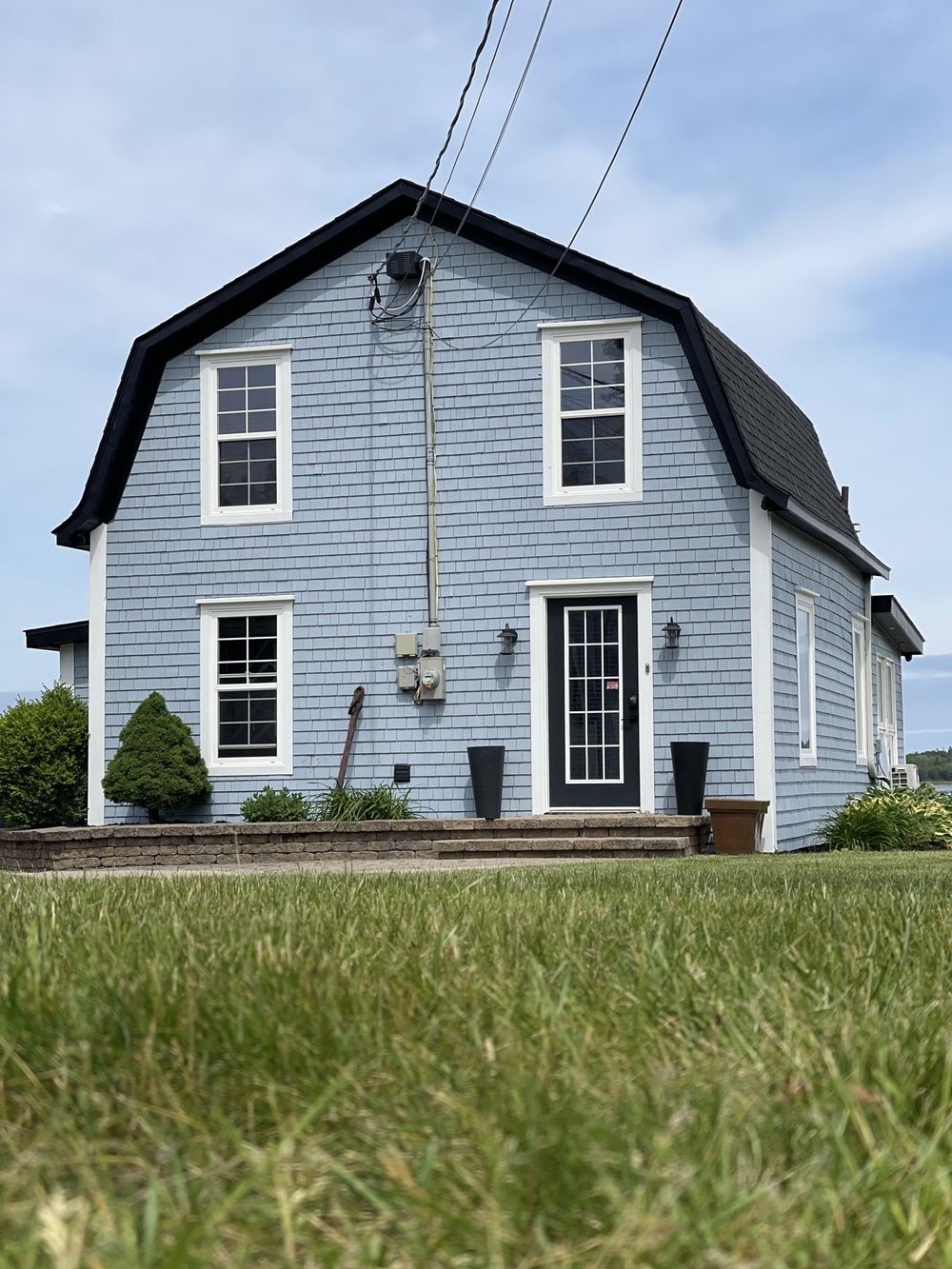 Front of a gambrel-roof cottage in Shediac freshly repainted in light blue with white trim and a black door