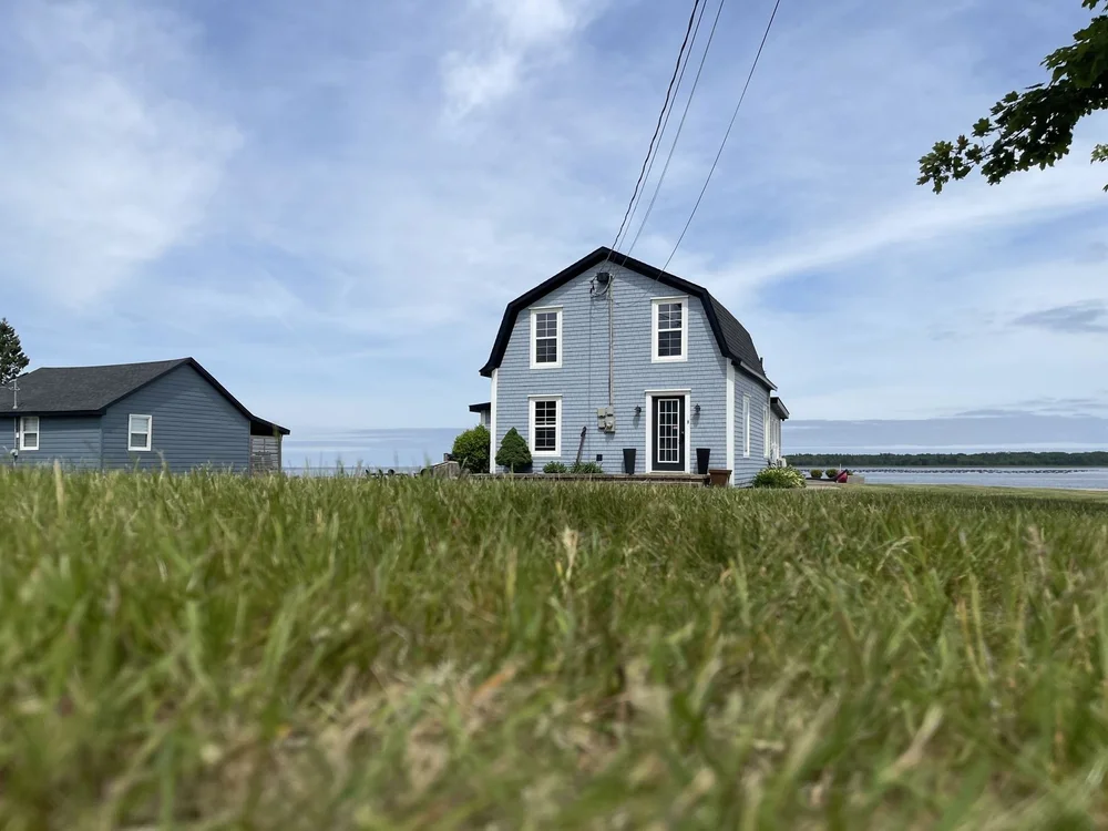 Light blue repainted cottage on a grassy lot overlooking the shore in Shediac, NB