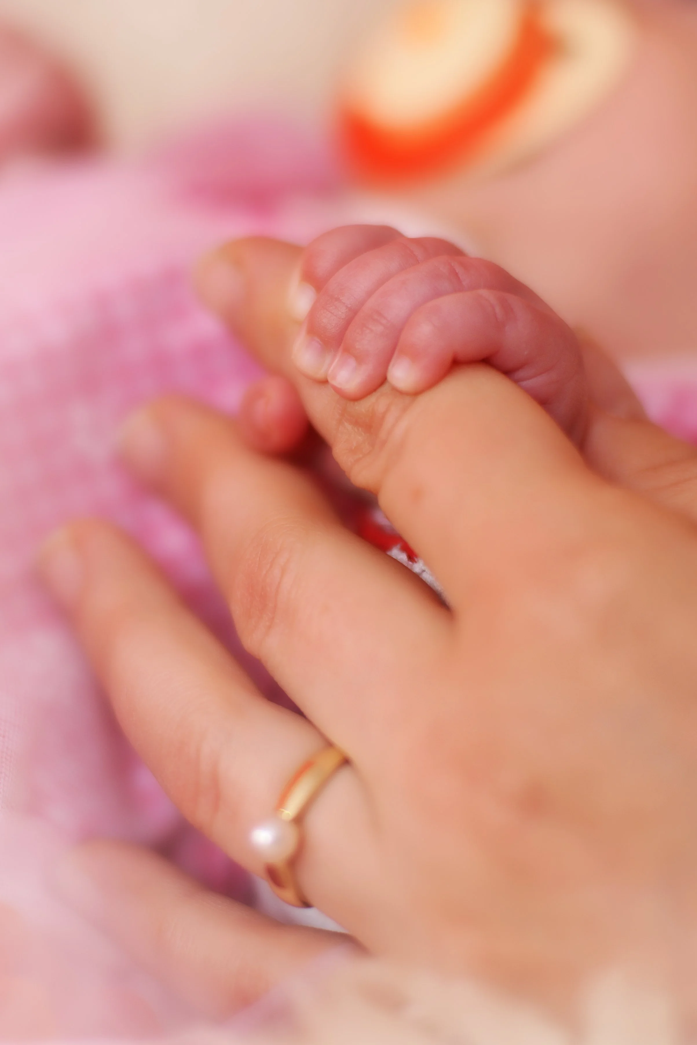 Nahaufnahme eines kleinen Babys, das eine Hand einer erwachsenen Person hält.